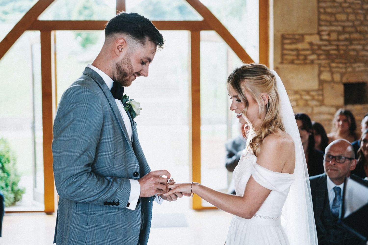 A couple exchanges rings during their wedding ceremony in a beautiful stone chapel with arched windows.