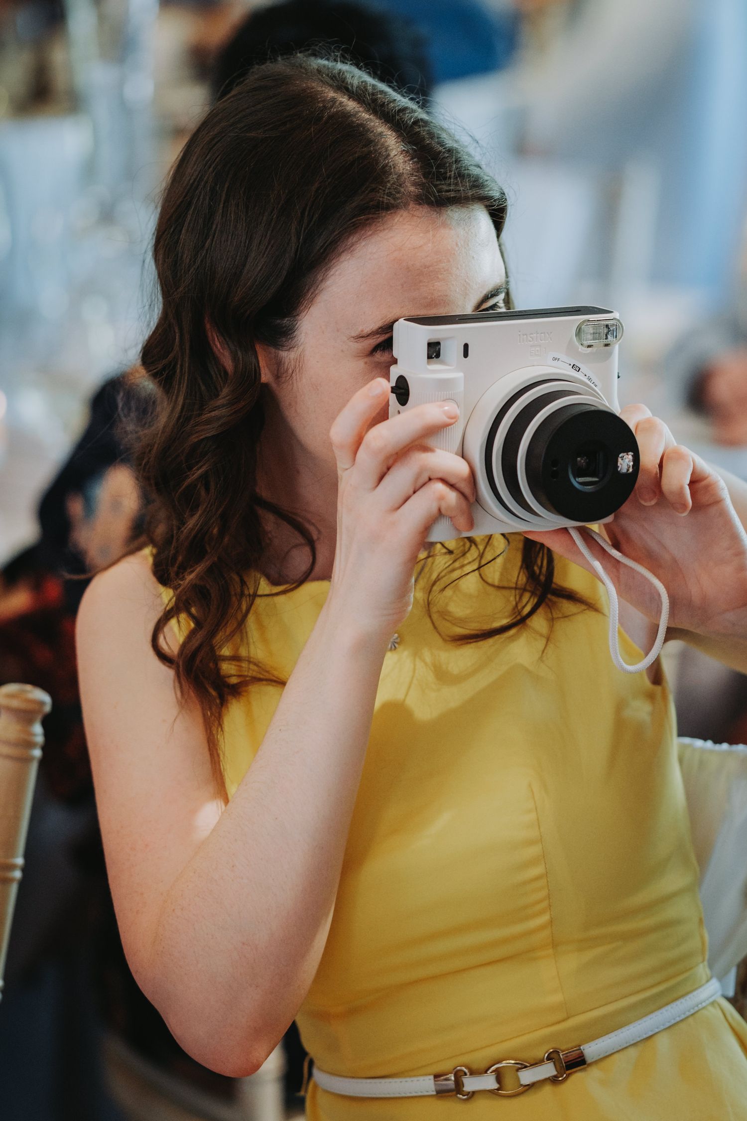 A wedding guest in a yellow dress takes a picture with a white instant camera.