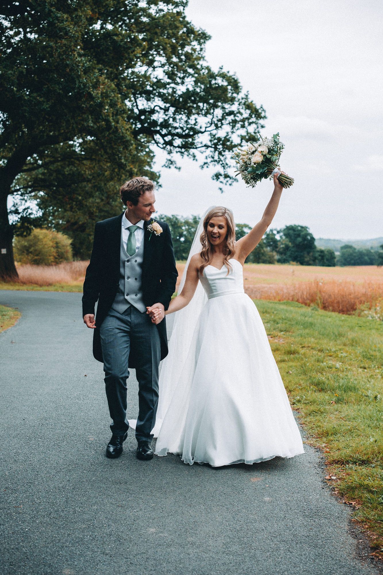 Newlyweds walking together on a path surrounded by autumn scenery.