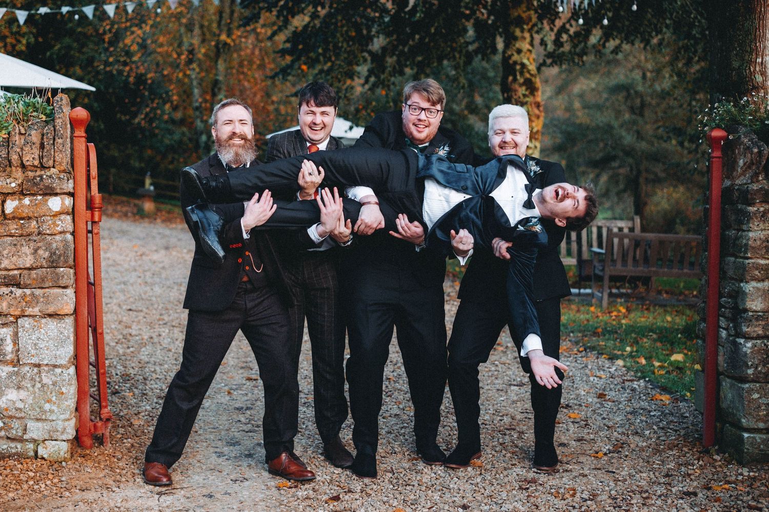 Wedding party posing playfully outdoors with bunting decorations visible in background.