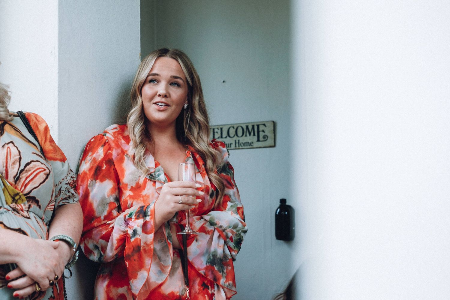 Guests in colorful floral dresses gather in a bright indoor hallway.