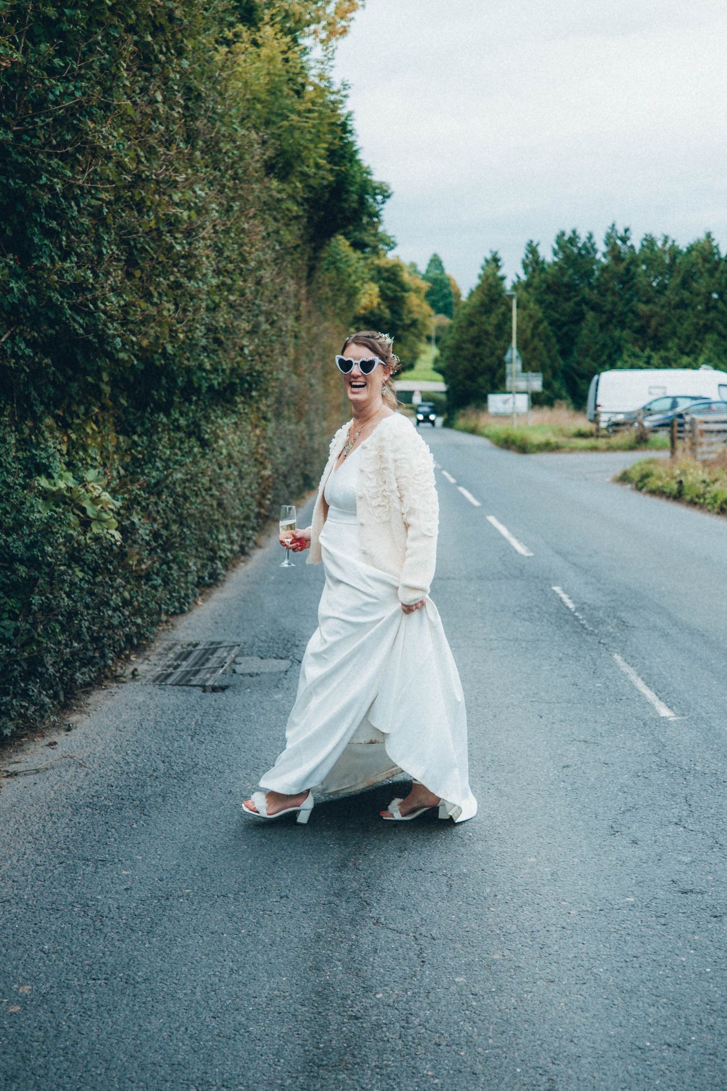 People in formal attire pose playfully on a rural road during a wedding photoshoot.
