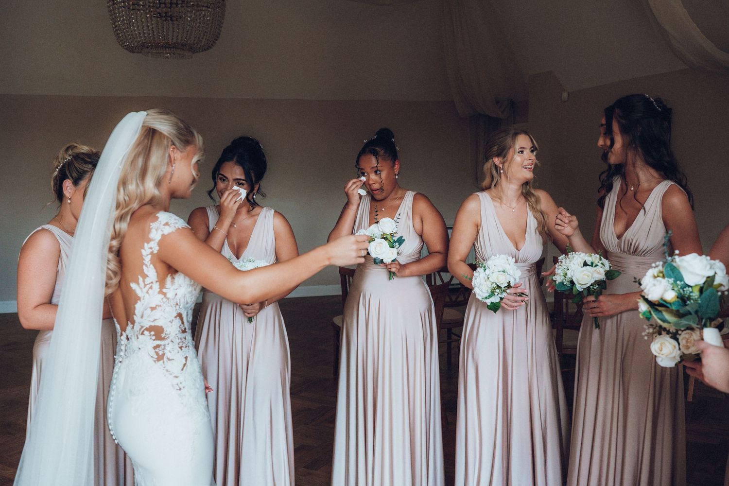 Row of bridesmaids in neutral dresses during wedding ceremony preparations.