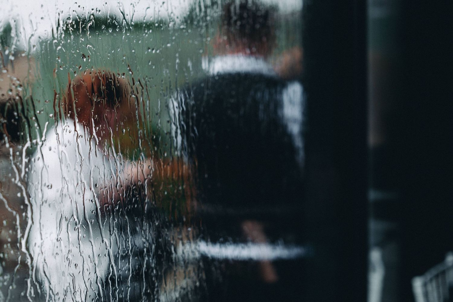Blurred silhouettes visible through wet glass with water droplets creating an abstract, moody atmosphere.