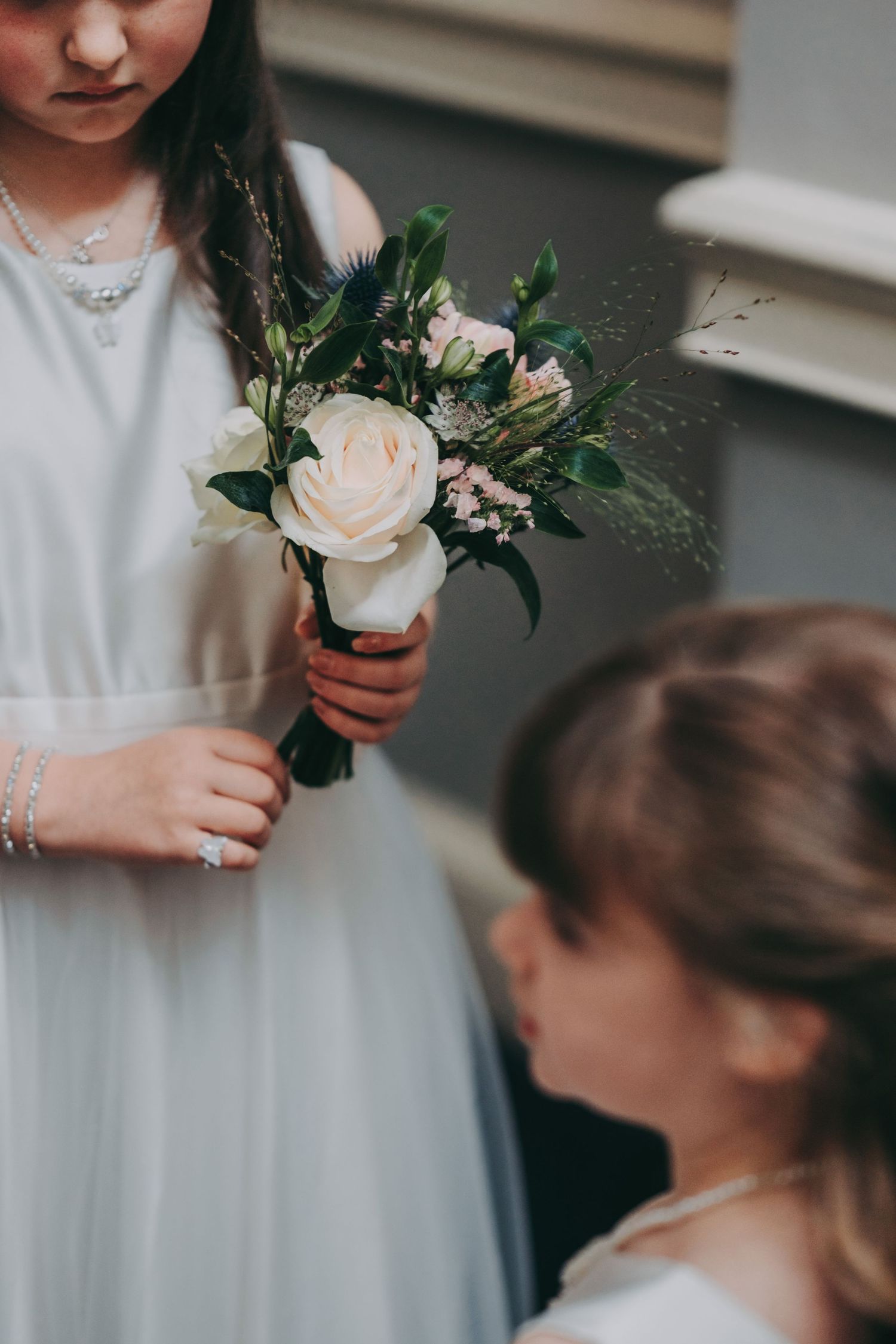 Close-up of white rose bouquet held by attendants in white dresses at a wedding ceremony.