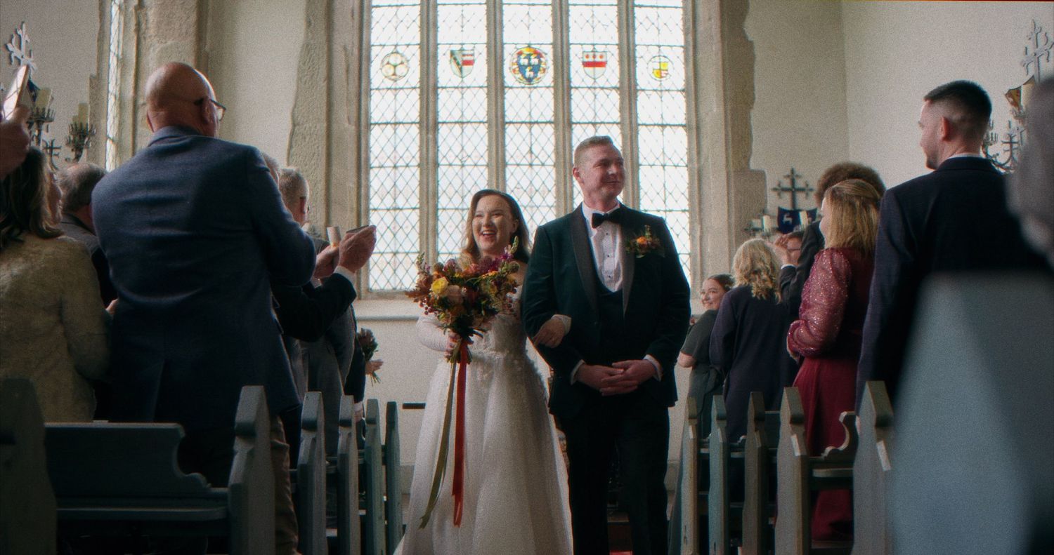 Wedding guests gather in a historic church with stained glass windows during an intimate ceremony.