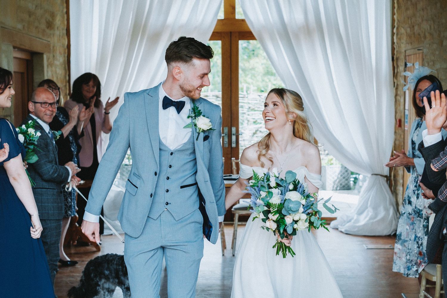 A couple shares a joyful moment during their wedding ceremony in an elegant venue with white curtains and floral decor.