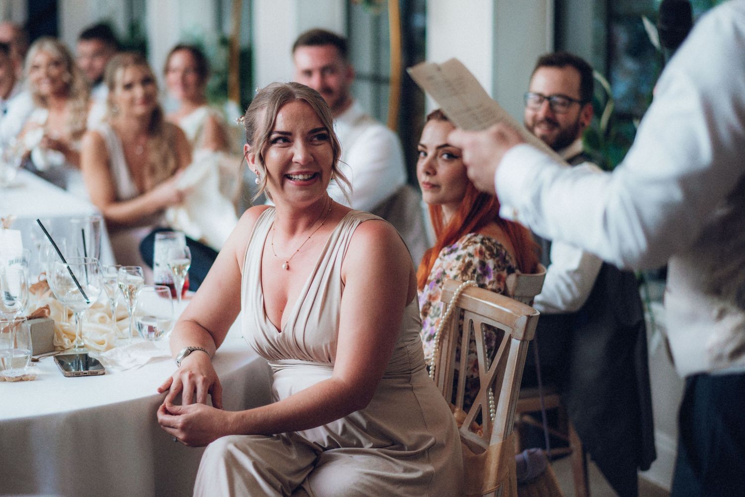 Wedding guests react with laughter during reception speeches at decorated indoor venue.
