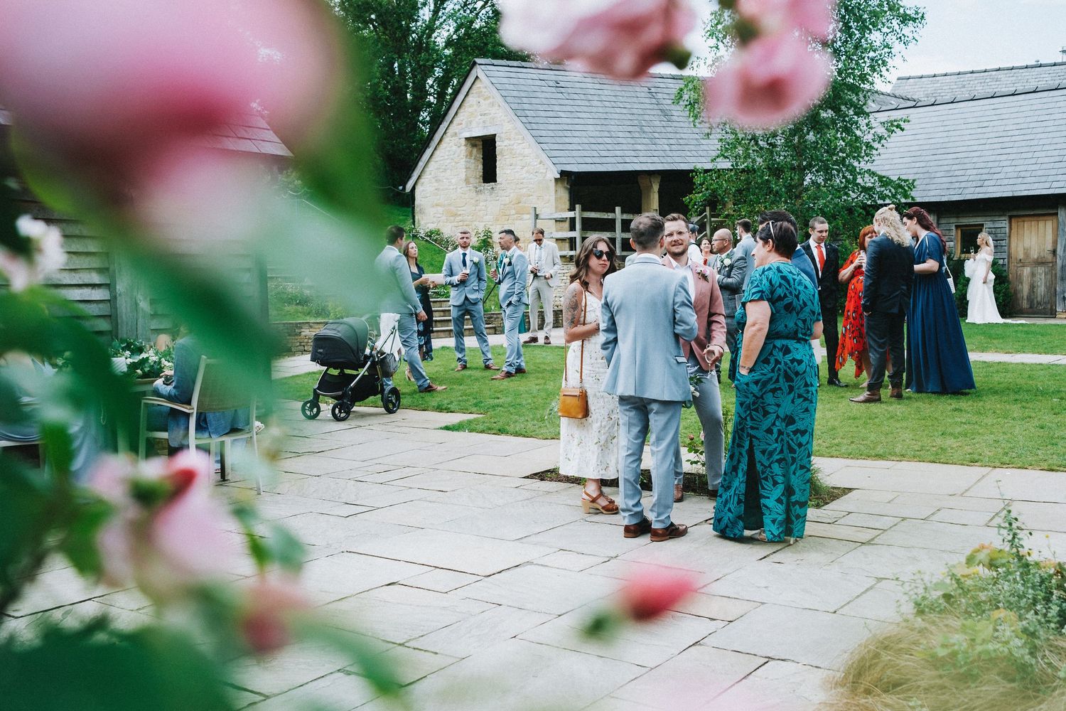 Guests mingling at an outdoor wedding venue with blooming pink flowers in foreground.