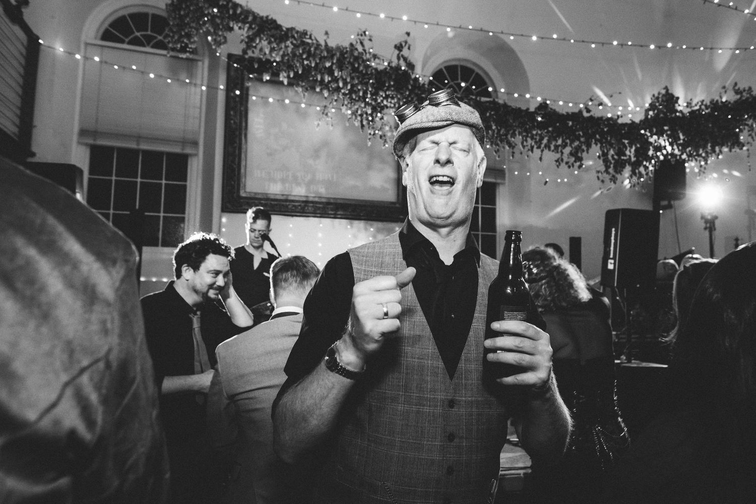 Black and white photo of a punk party guest celebrating under twinkling wedding lights.