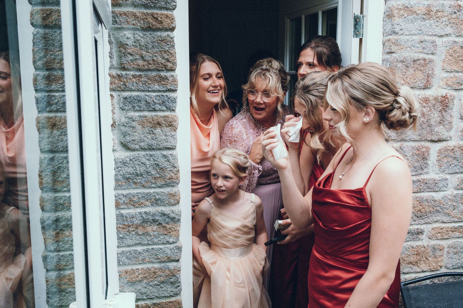 Large group photo of wedding guests in colorful dresses seated outdoors.