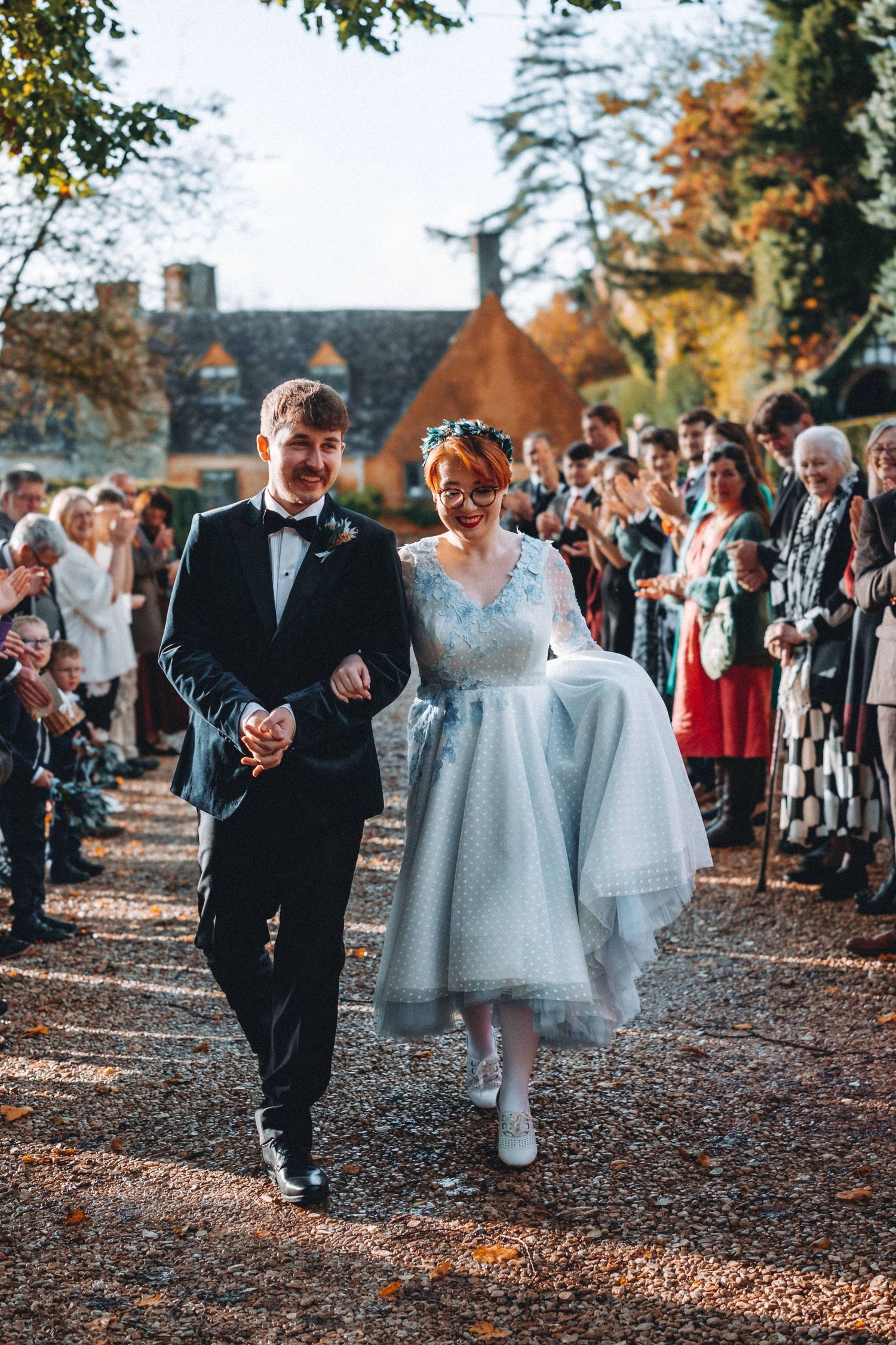 A wedding celebration in autumn with guests lining a tree-lined pathway as the couple passes by.