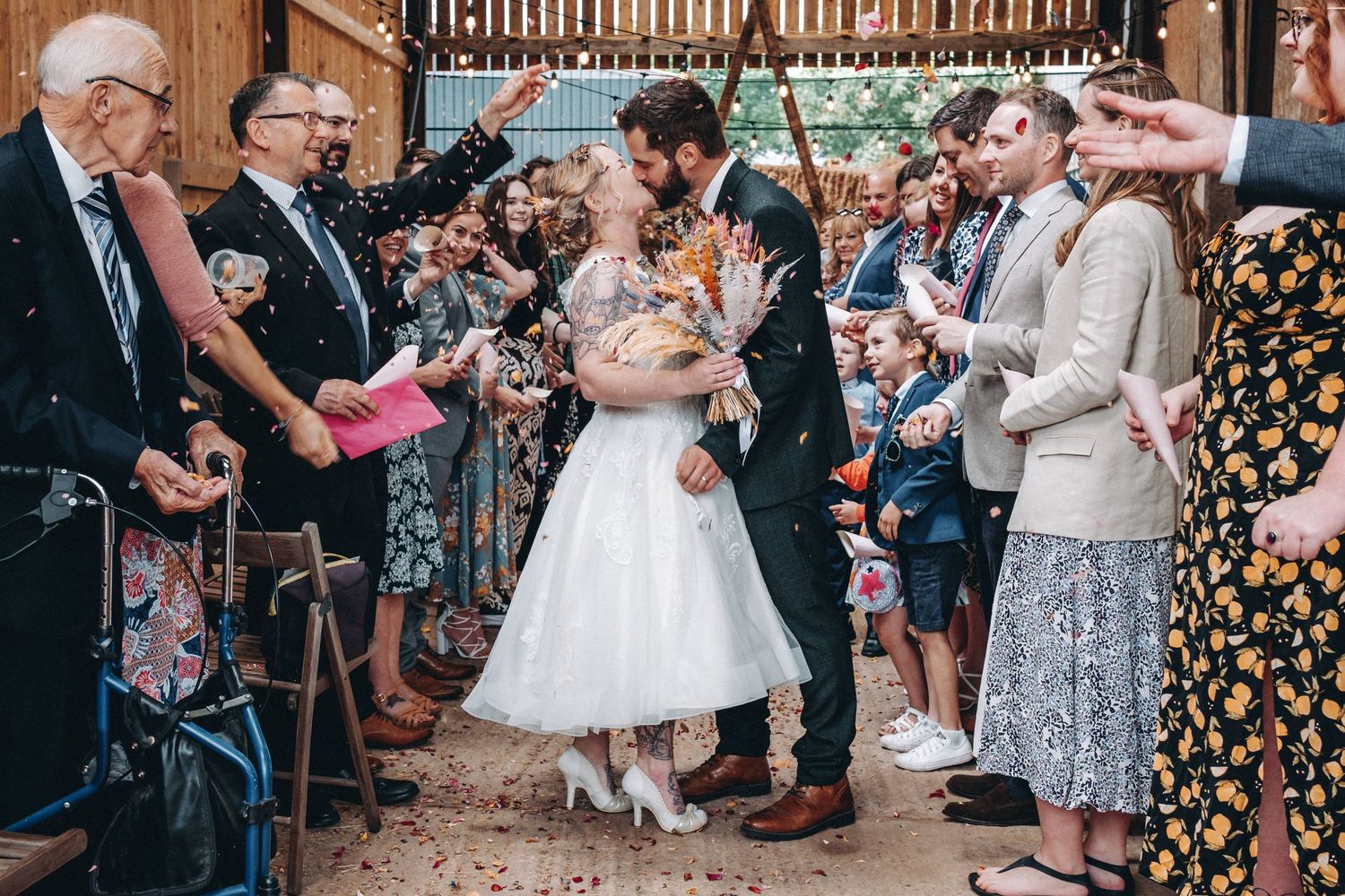 Wedding guests throw confetti over the couple during a vintage-style celebration with a bride in a tea-length white dress.
