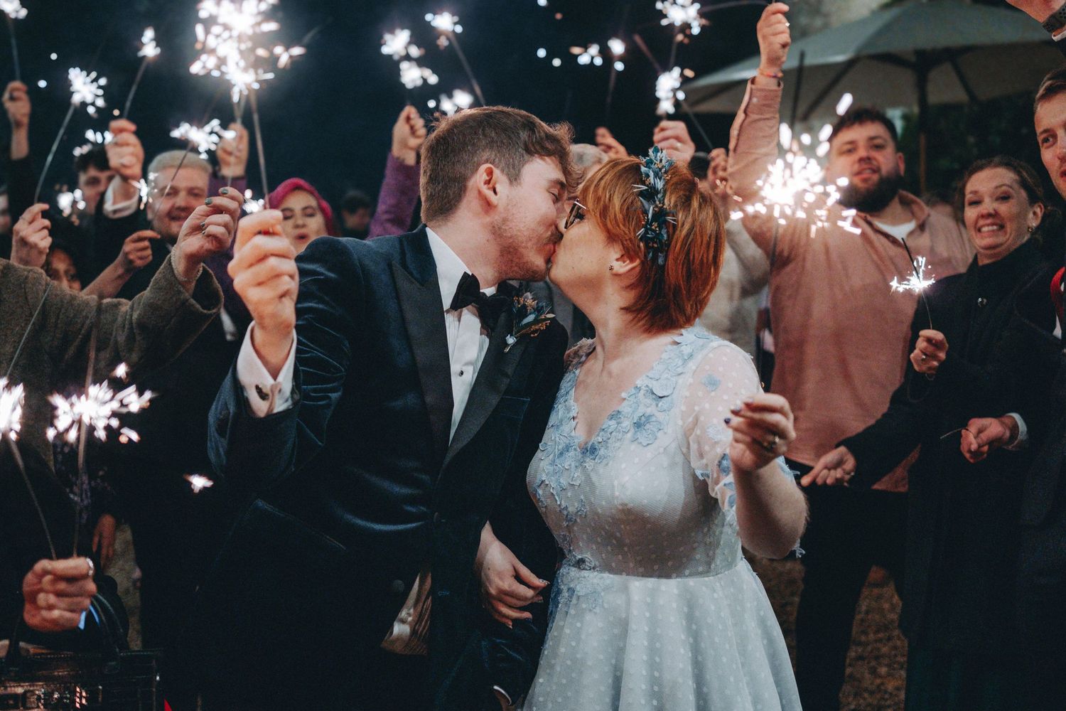 Romantic moment between newlyweds surrounded by guests holding sparklers in the evening.