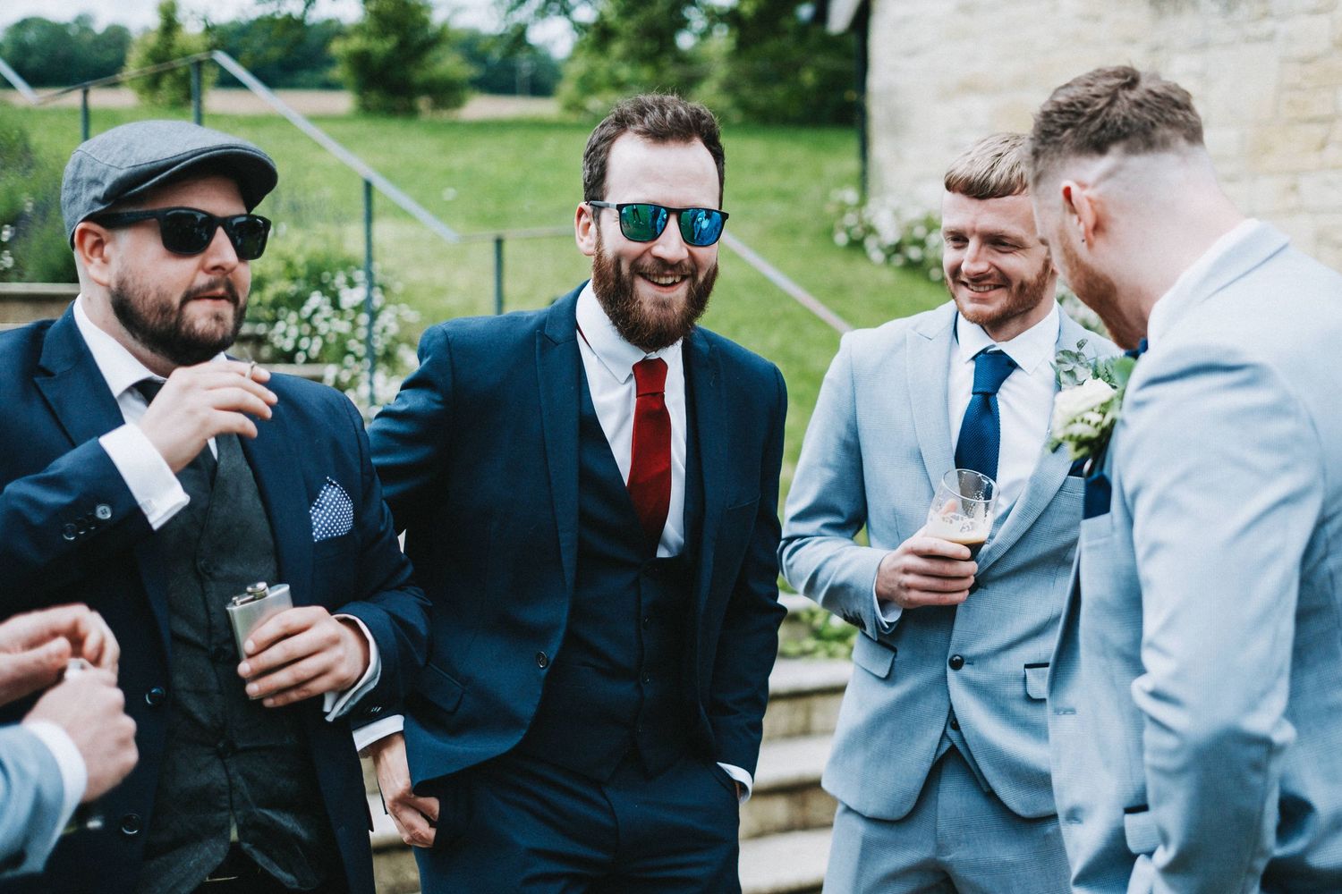 A group of well-dressed guests sharing drinks and laughs at an outdoor wedding event.