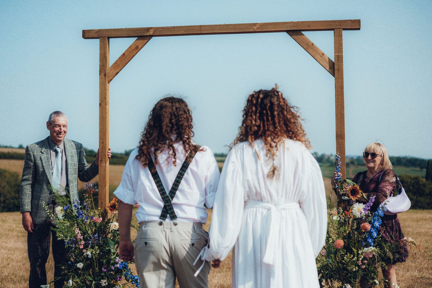 Rustic wooden wedding arch stands against blue sky in outdoor ceremony setting.