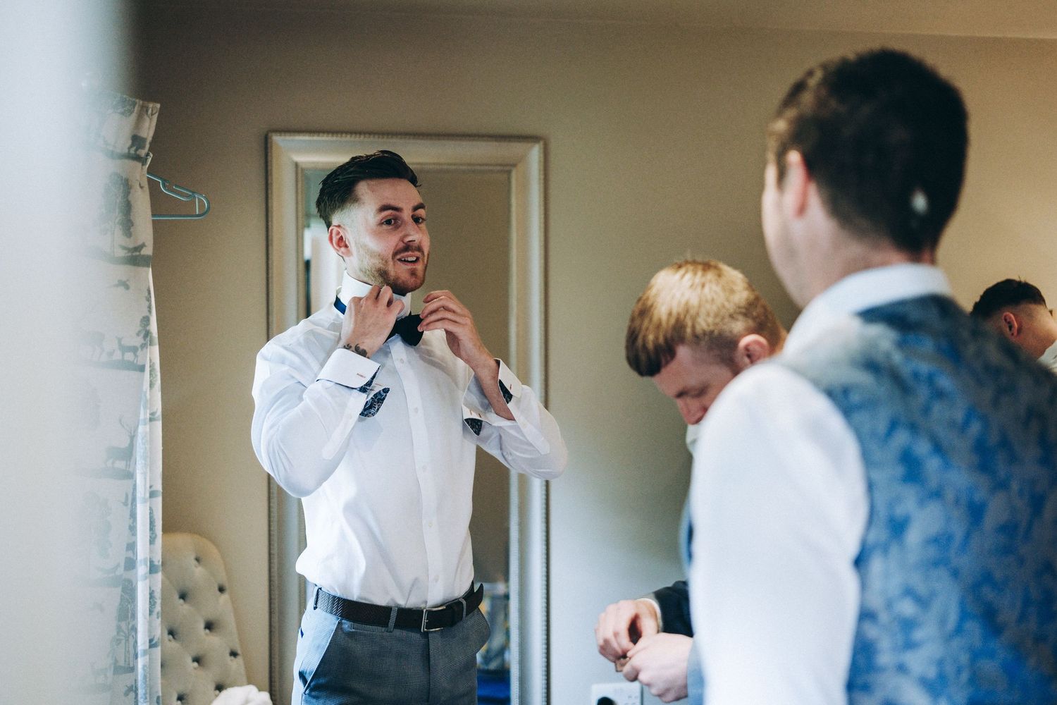 Wedding party members helping with formal attire preparations in a getting ready room.
