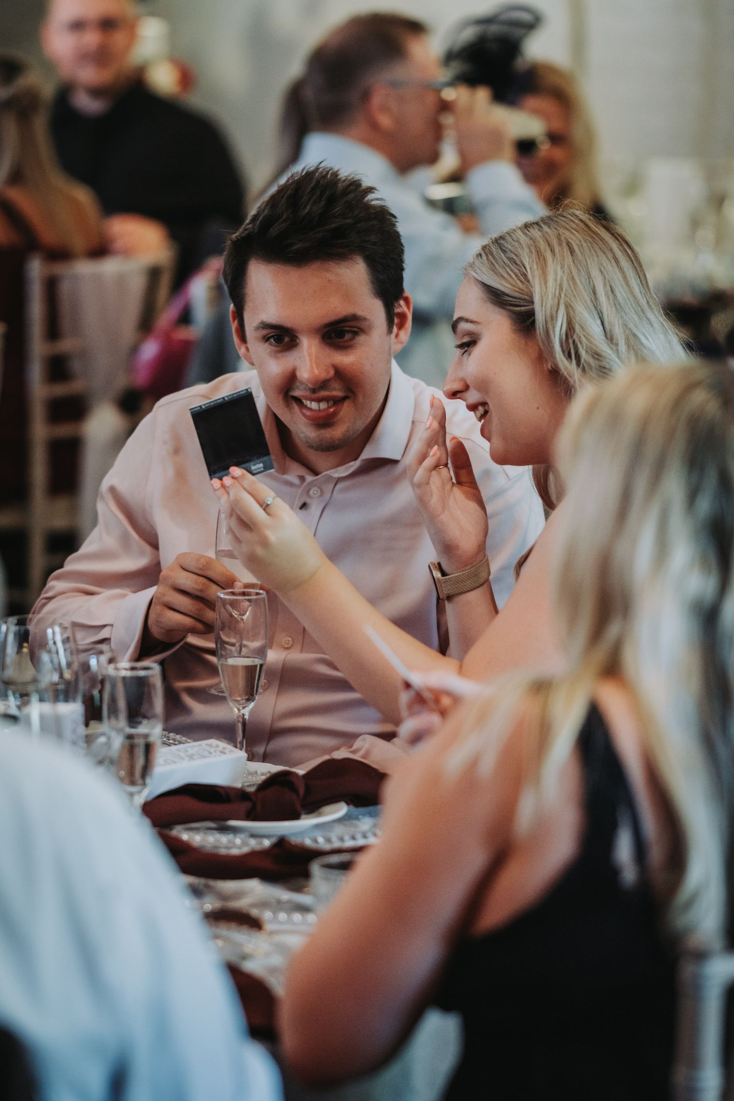 Wedding guests share a laugh during dinner reception at elegant table setting with wine glasses.