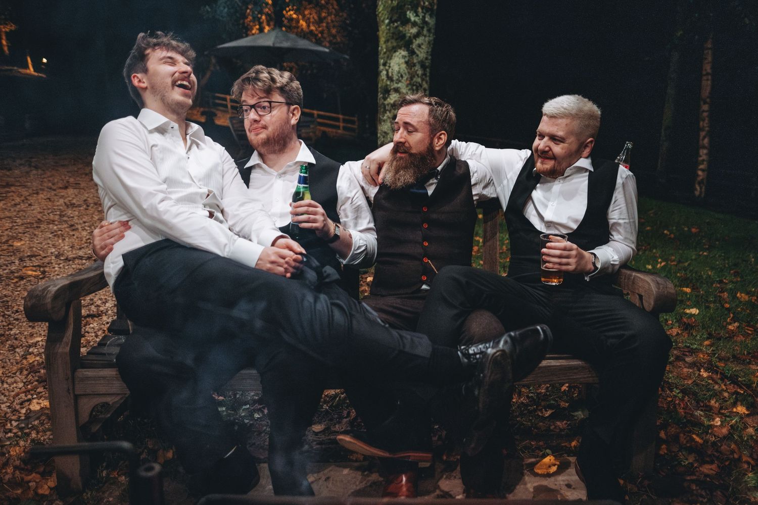 A group dressed in vintage attire sharing laughs while sitting on a wooden bench in autumn.