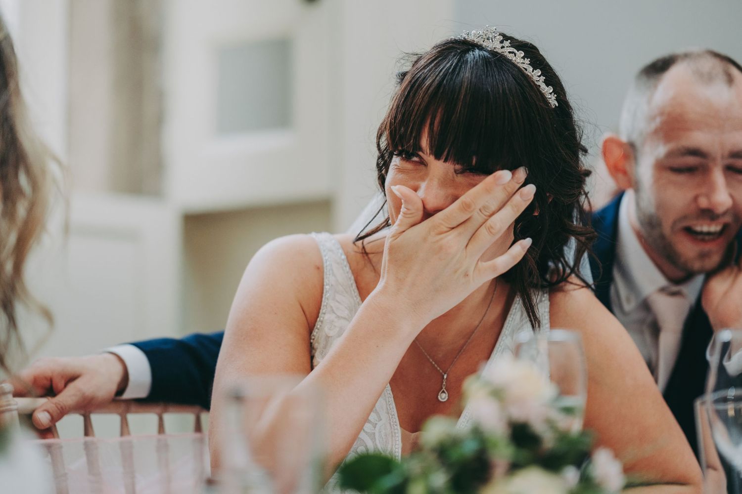 Joyful wedding reception moment showing genuine emotion and laughter during dinner speeches at elegant indoor venue.