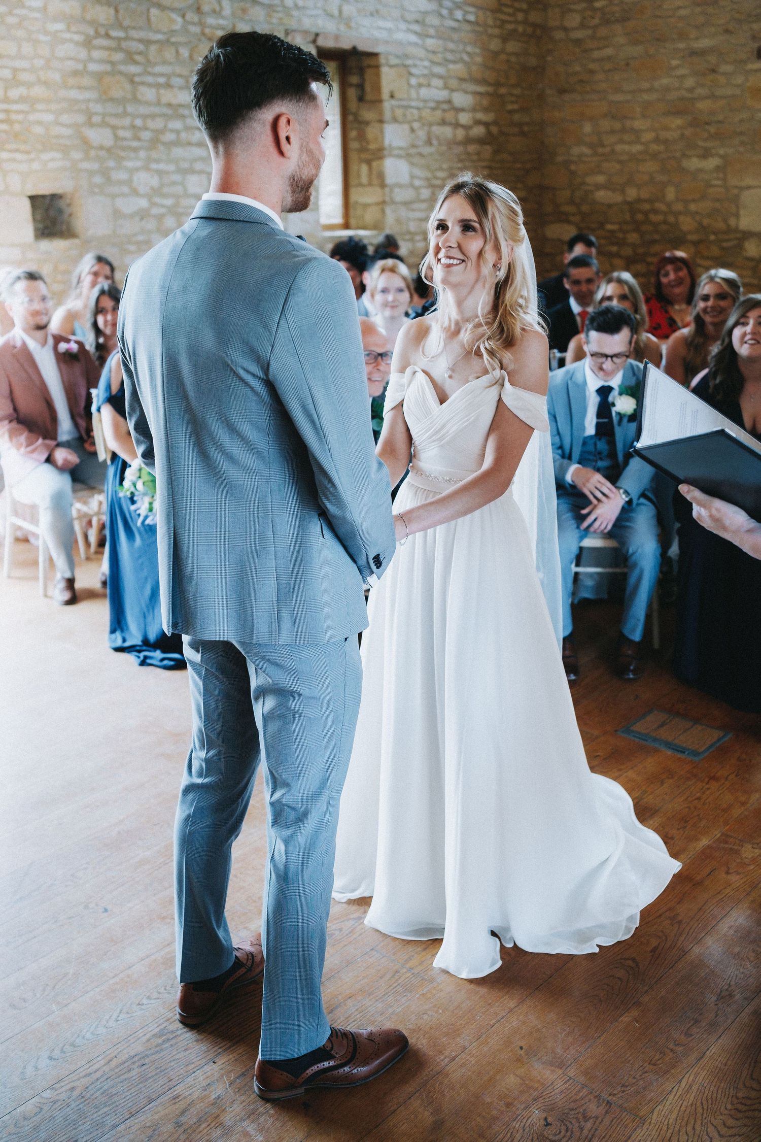 A joyful wedding ceremony in a rustic brick venue with a bride in white and groom in light blue suit.