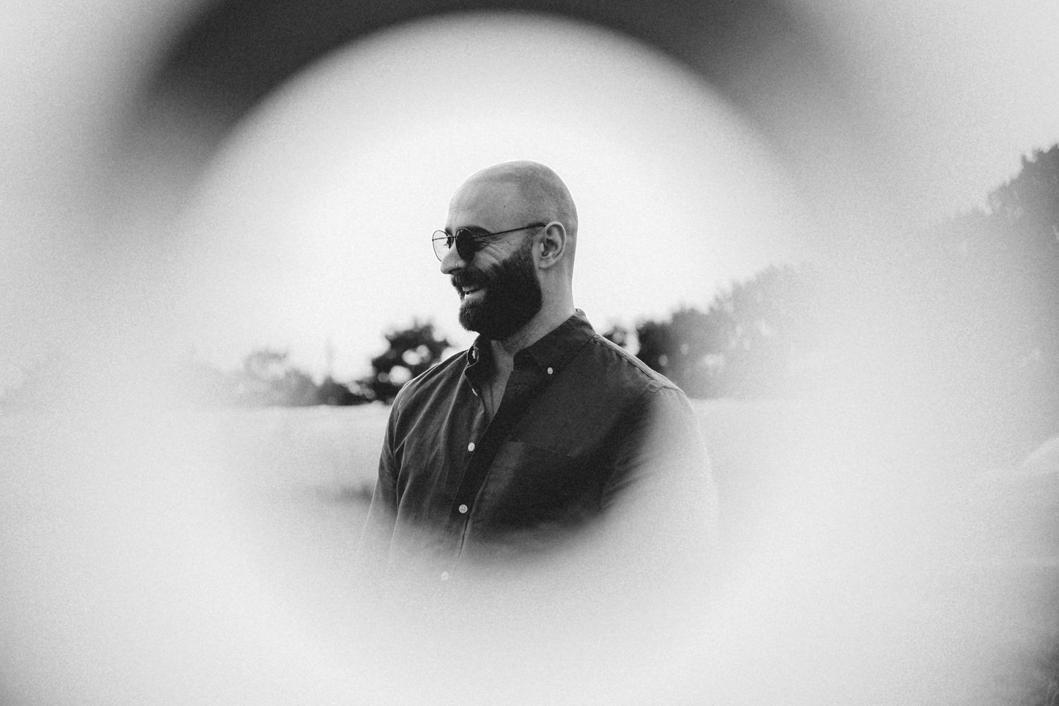 Artistic black and white portrait through blurred vignette showing a person in sunglasses and formal attire.