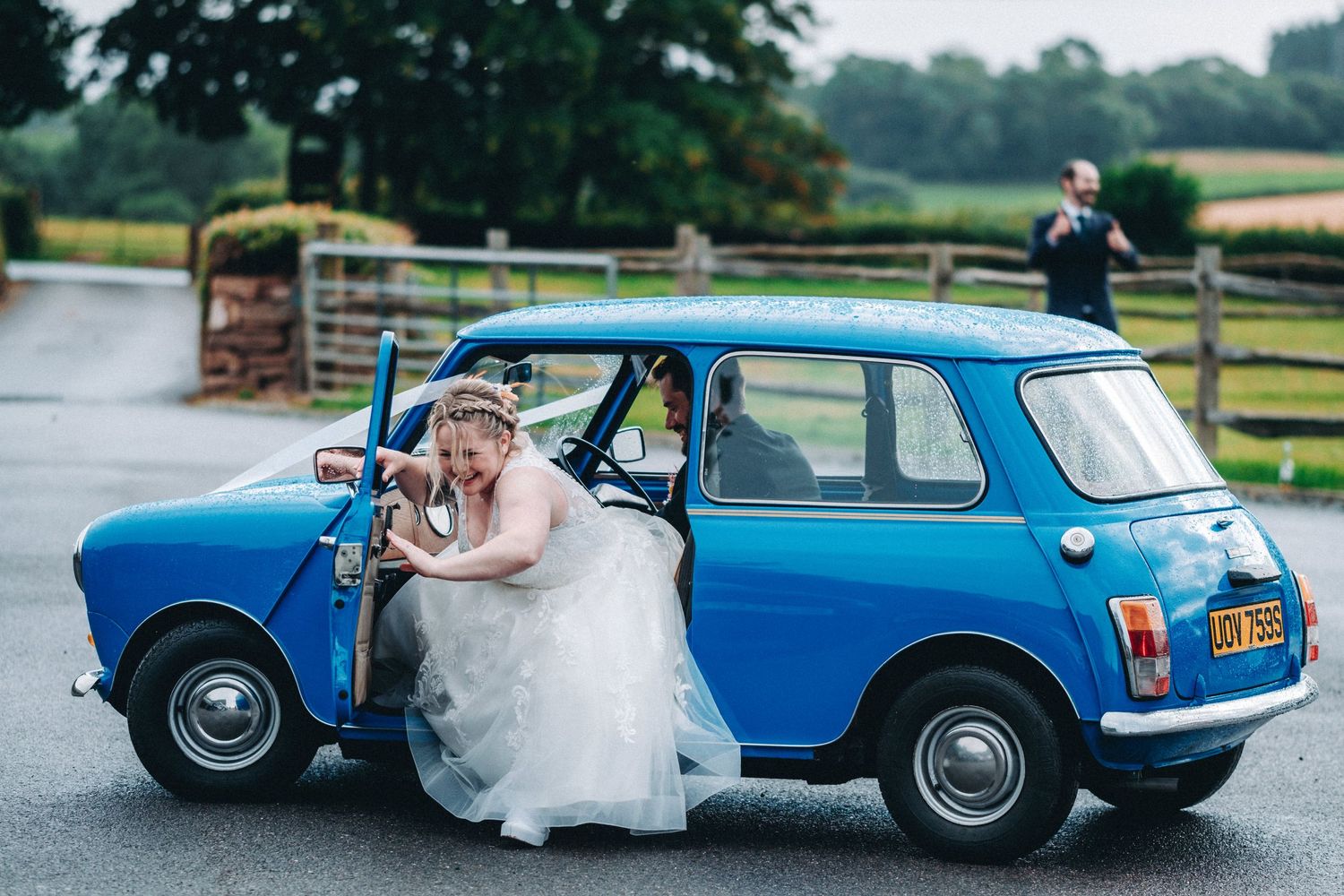 A bright blue vintage Mini Cooper parked on a rainy day at a countryside venue with countryside views. Bride trying to escape.