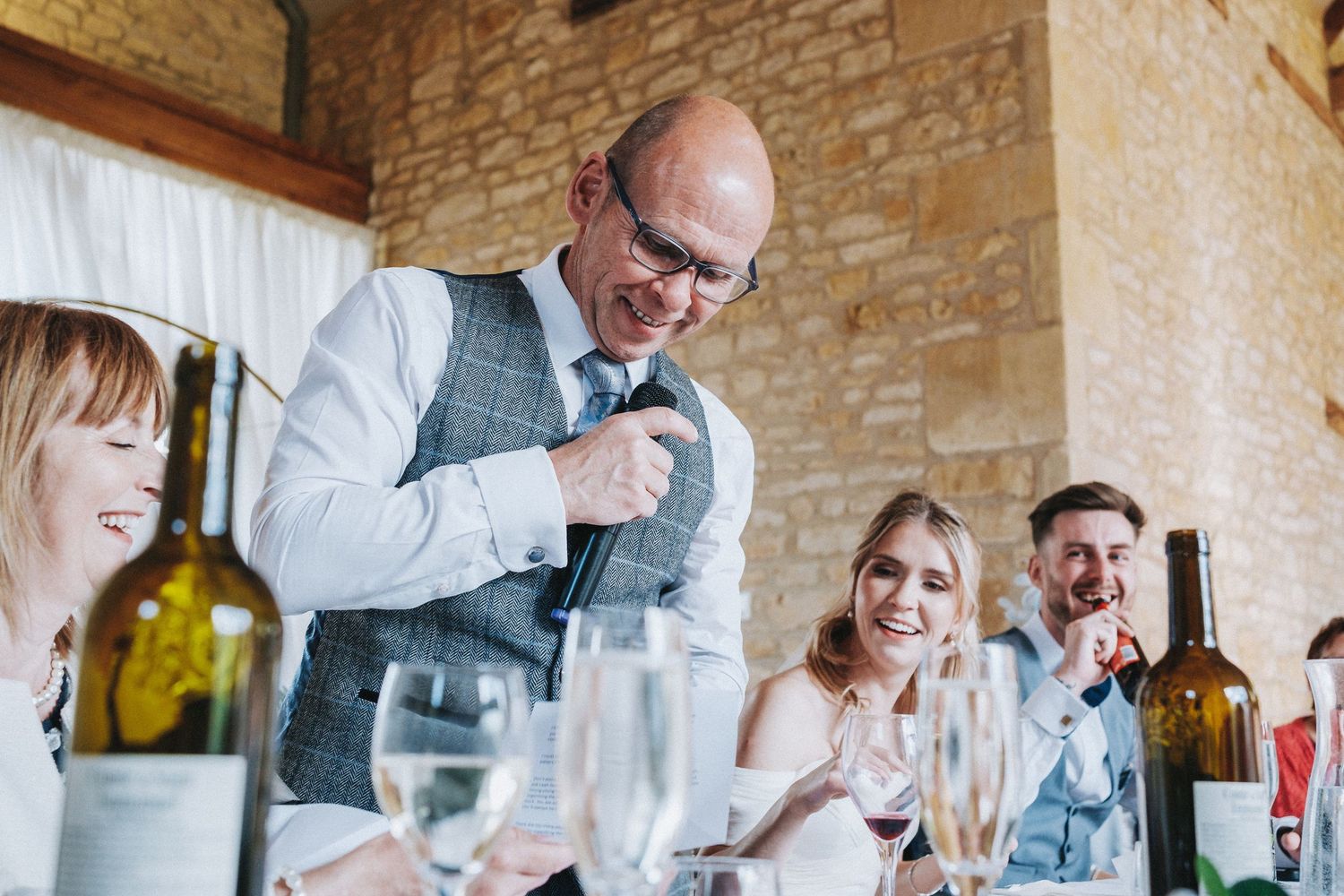 Guests enjoy lively conversation at elegant wedding reception with stone wall backdrop.