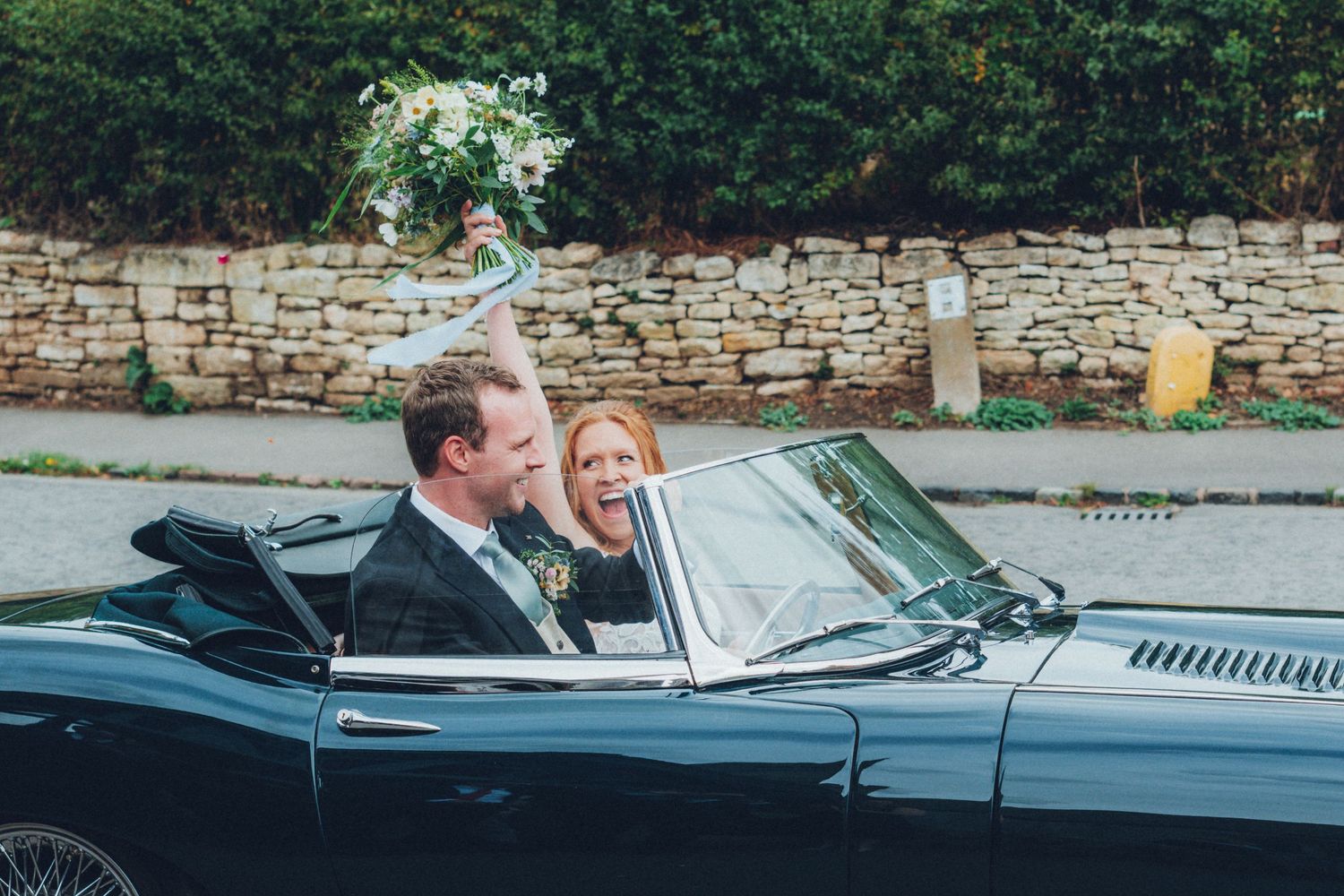 Classic vintage car parked outside stone building during wedding celebration.
