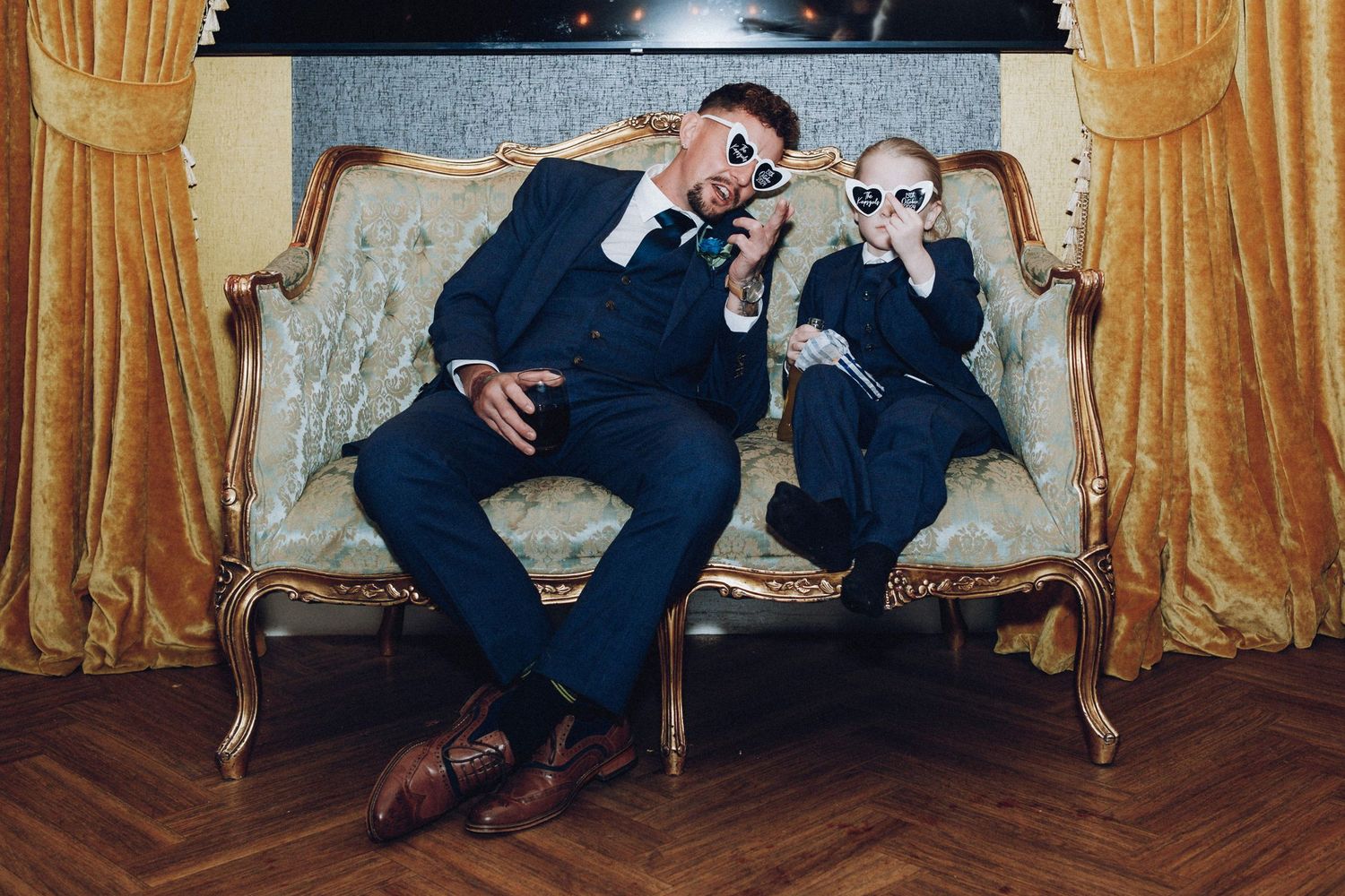 Wedding party members pose casually on vintage furniture with gold curtains in background.