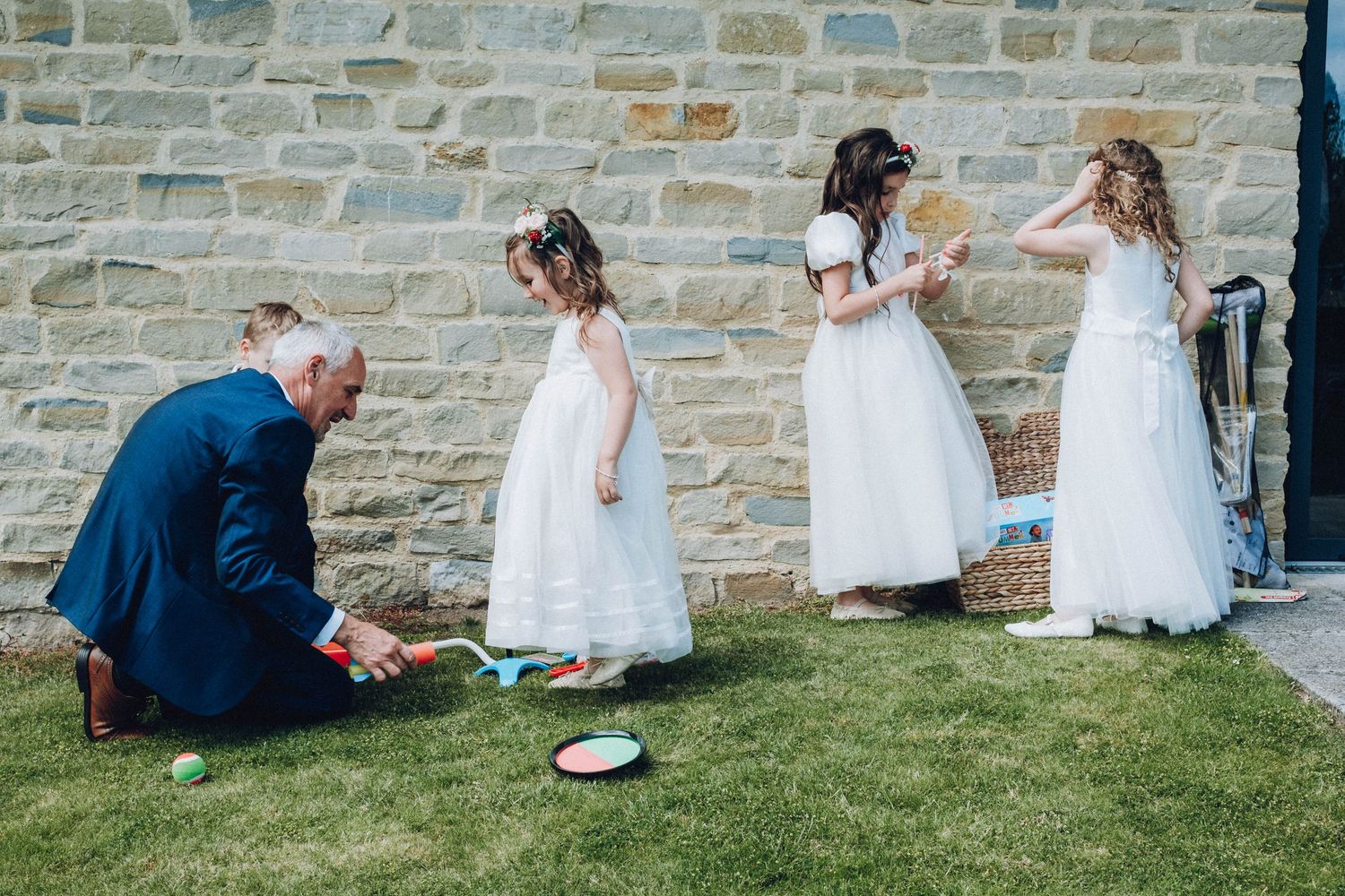 Wedding guests relax on a grassy lawn next to a stone wall during an outdoor reception.