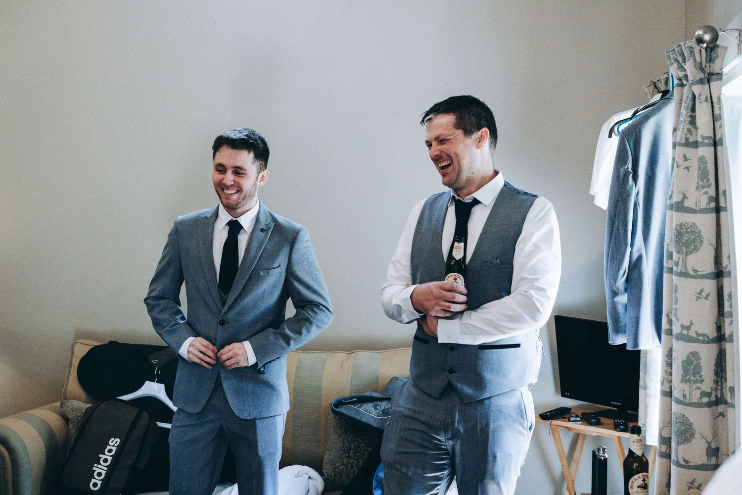 Two groomsmen sharing laughter while getting ready in formal wear before the wedding ceremony.