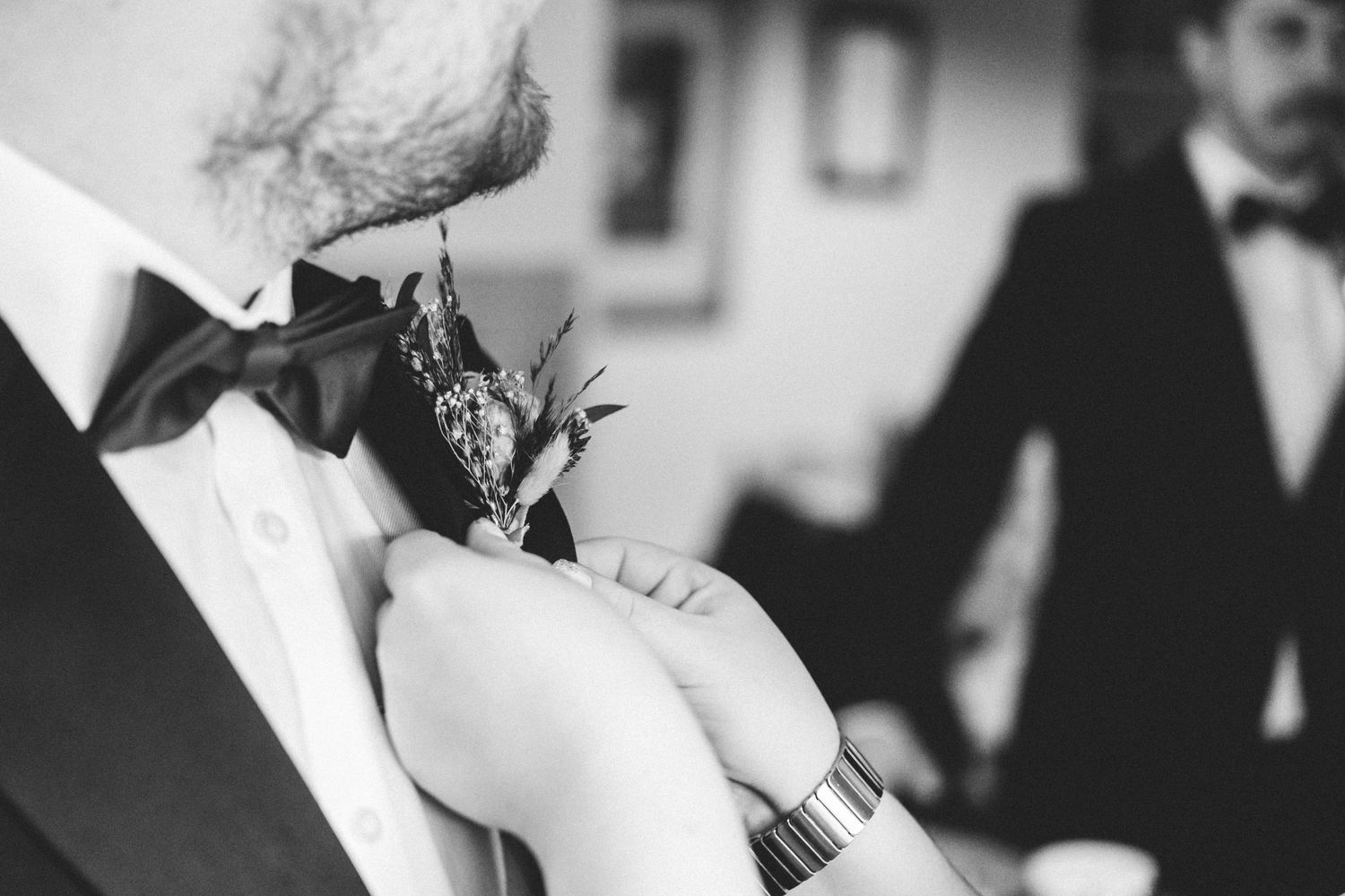 Someone pins a buttonhole flower to a groomsman's tuxedo lapel at a wedding.