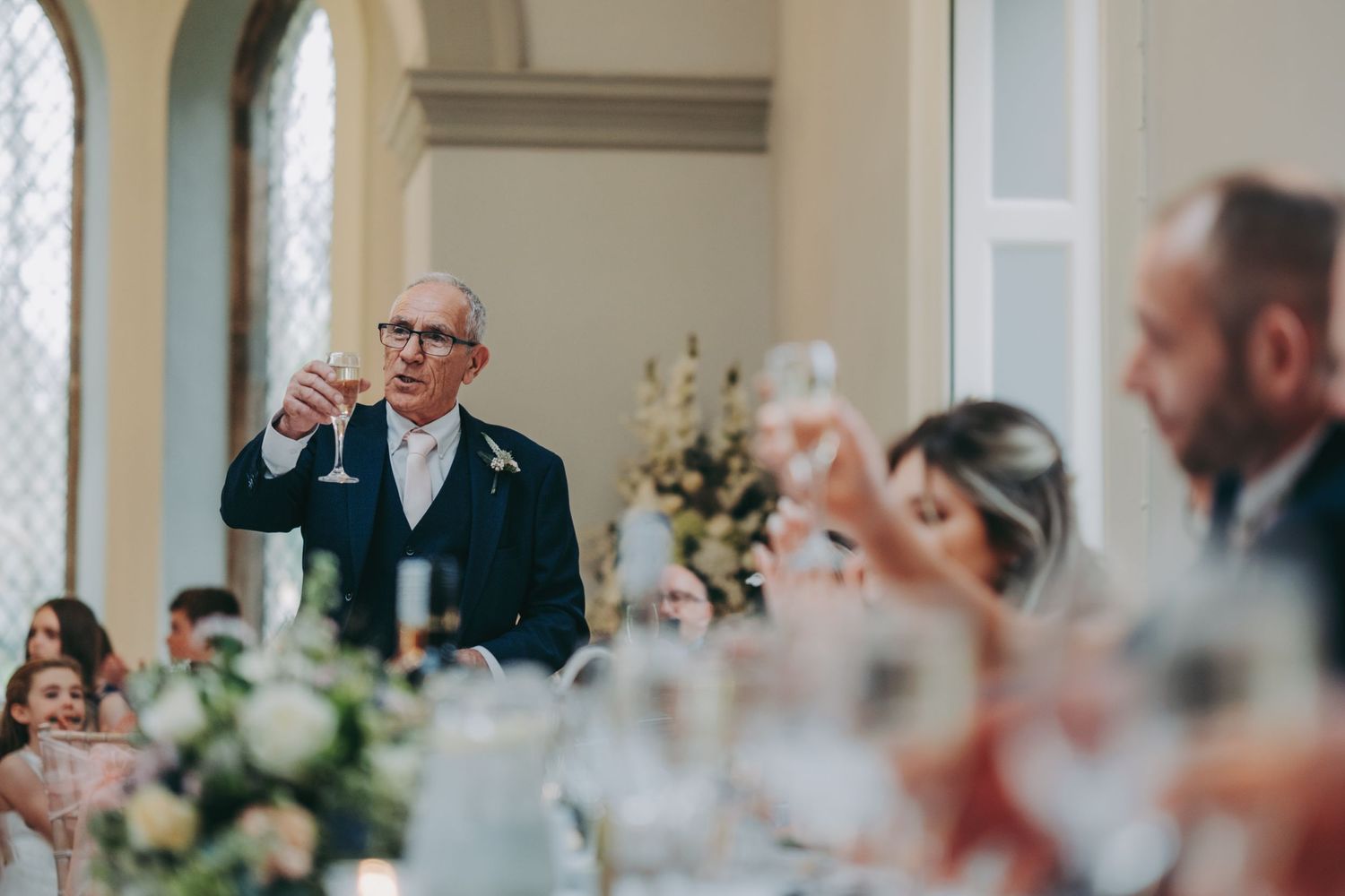 Toast being raised during wedding reception with elegant floral centerpieces.