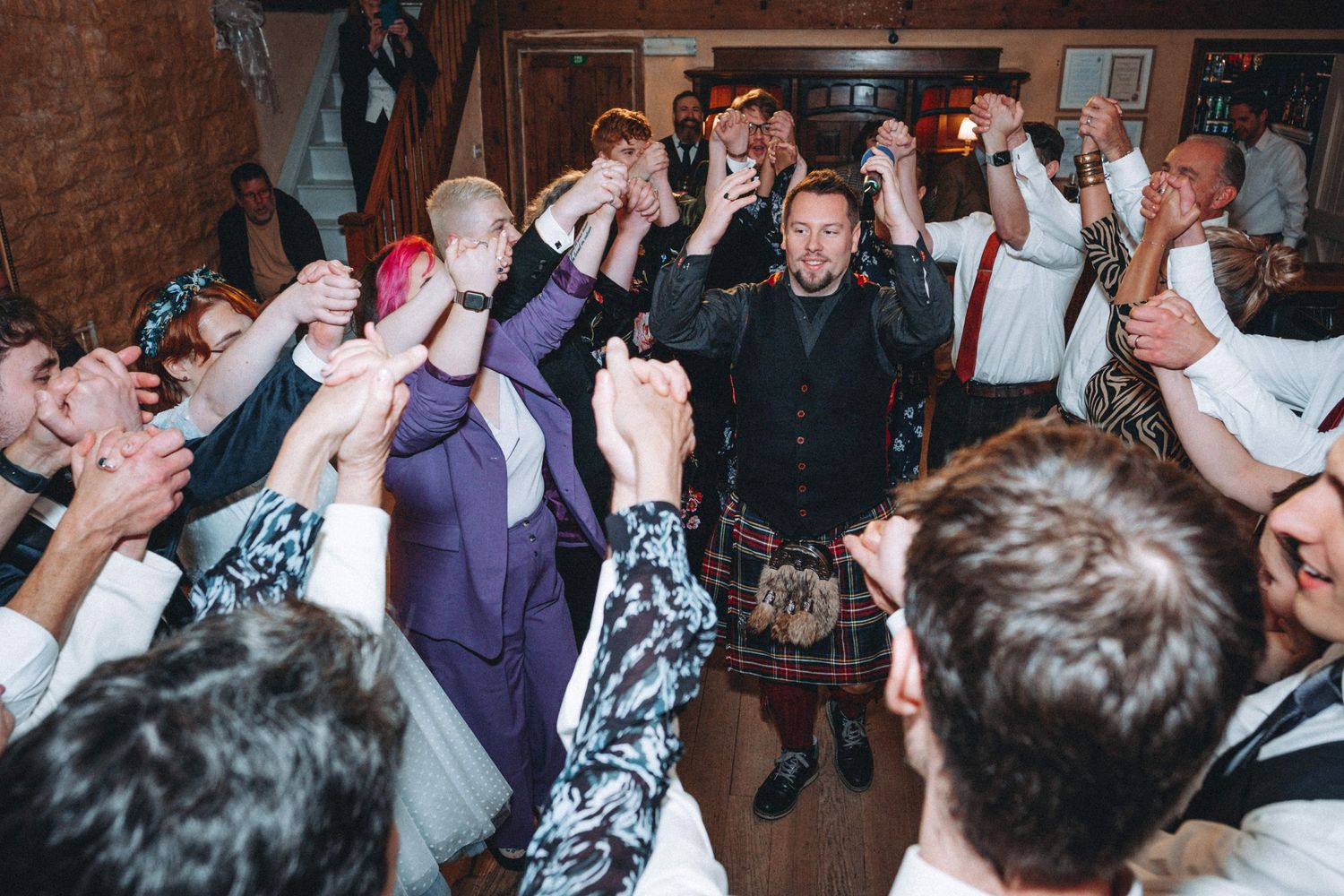 Energetic dance party scene at wedding reception with guests raising hands in celebration.