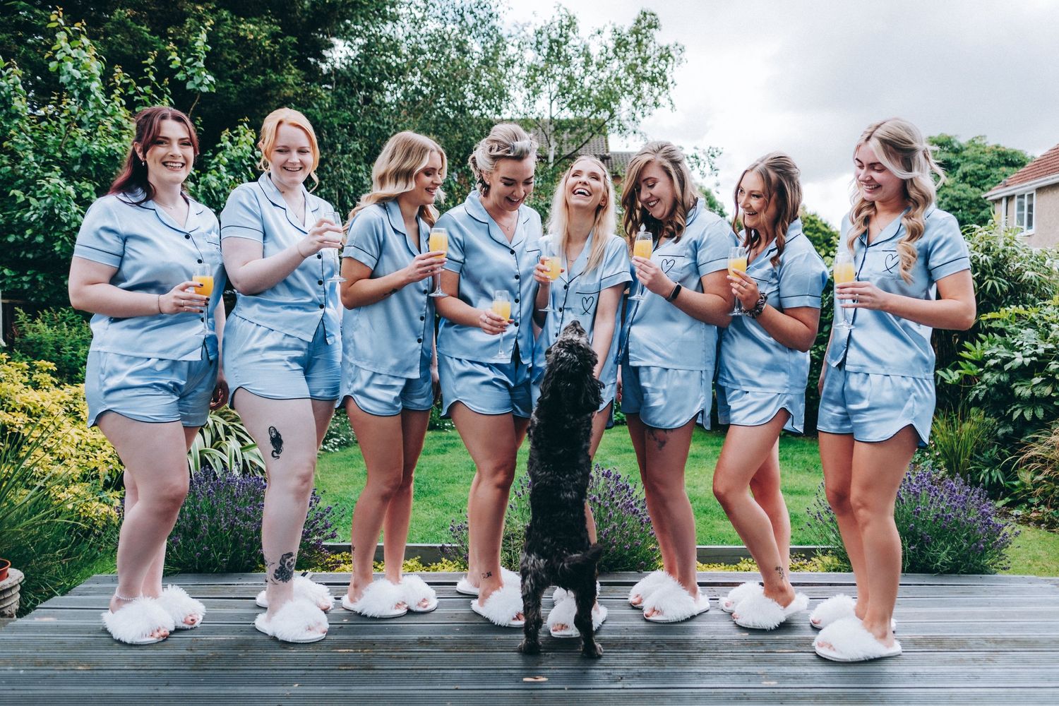 Bridesmaids in matching blue pyjamas pose together with a Leah's dog Nala on outdoor deck.