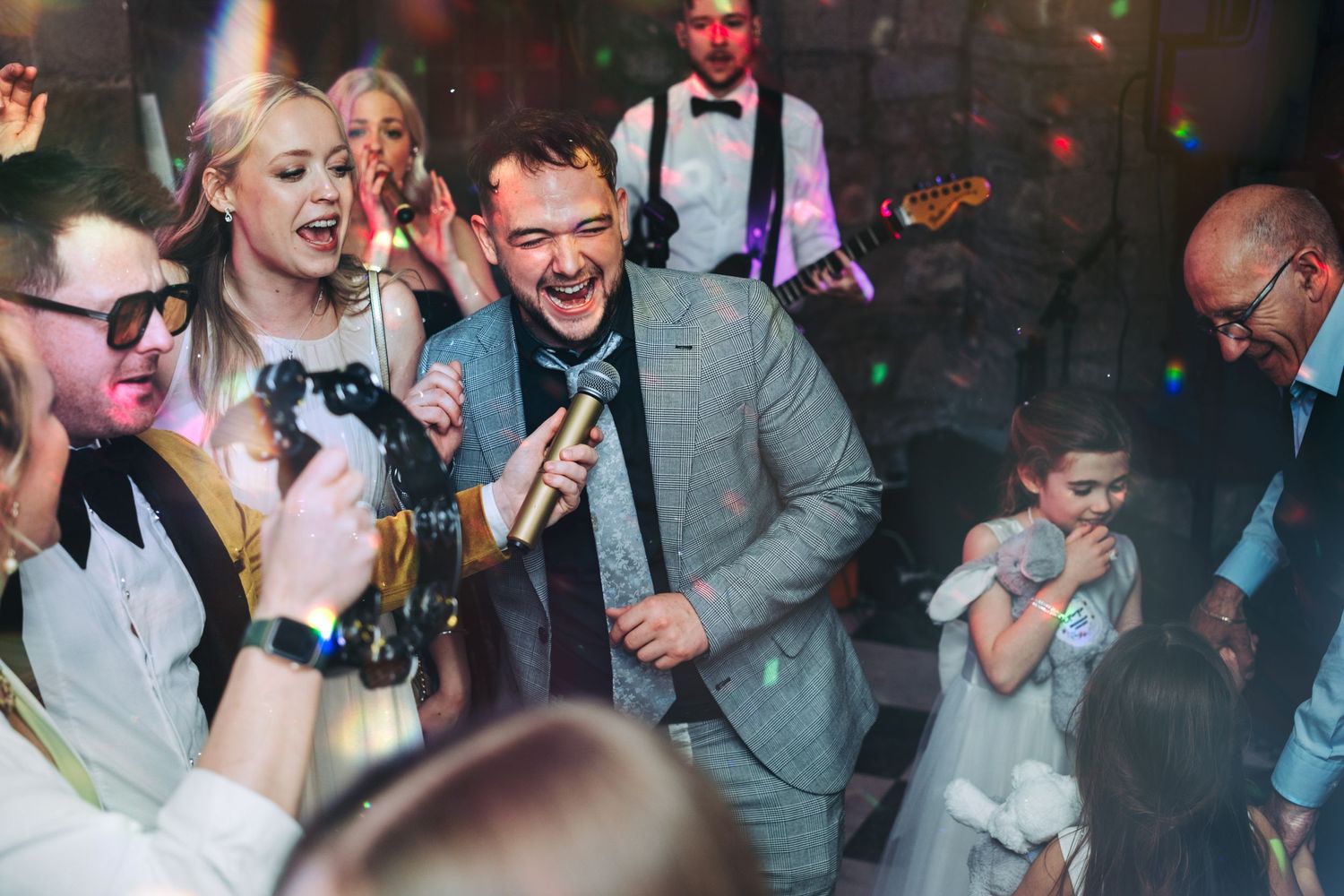 Enthusiastic celebration on wedding dance floor with guests cheering and dancing.