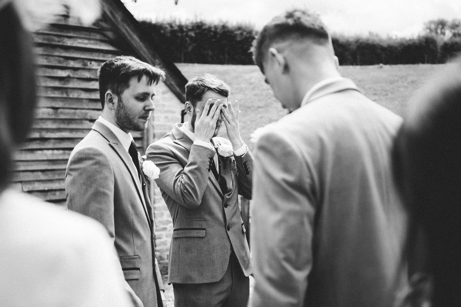 A candid black and white photograph showing men in suits gathered outdoors near wooden steps.