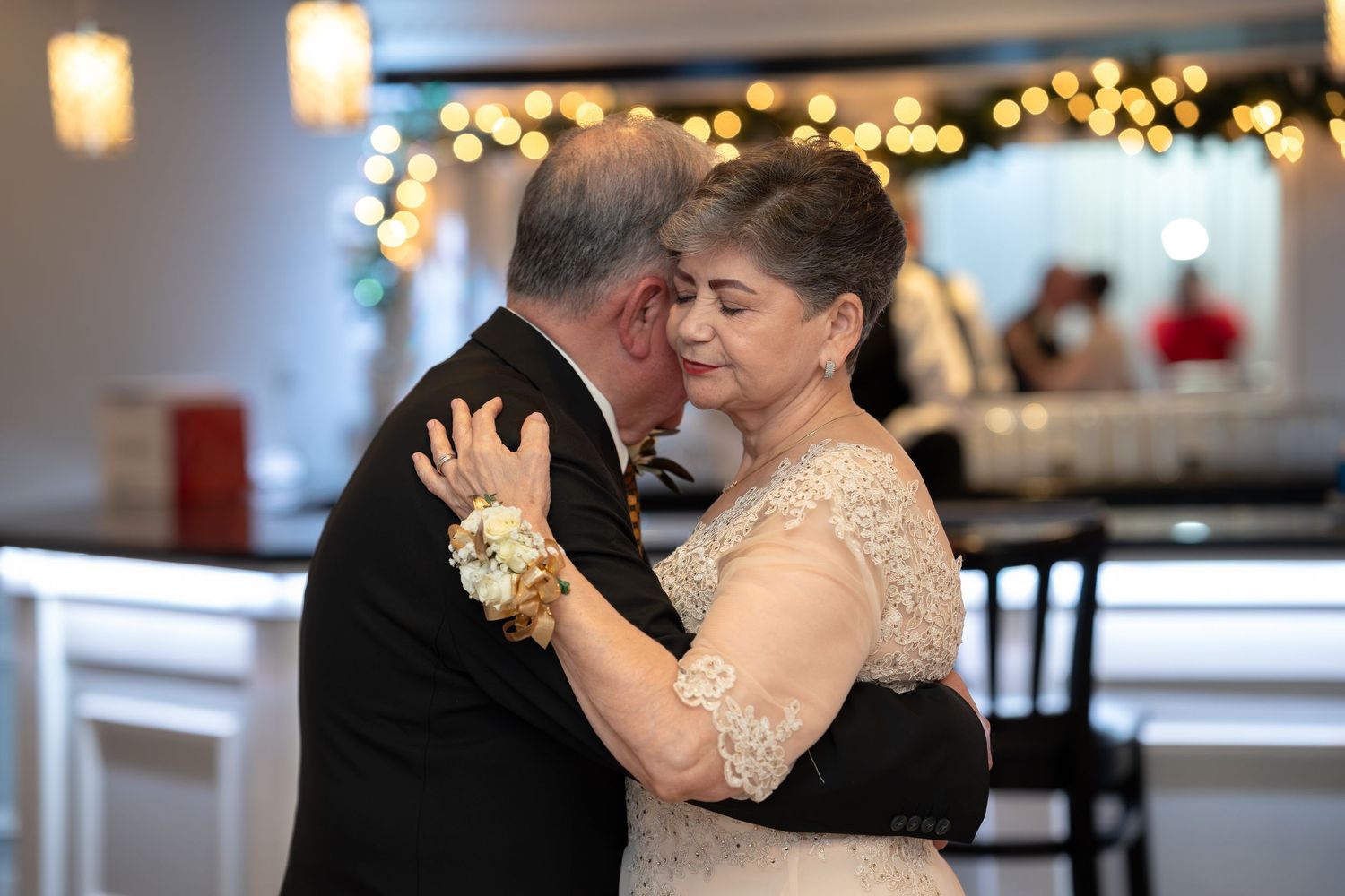 Older couple shares intimate slow dance embrace in warmly lit reception venue.