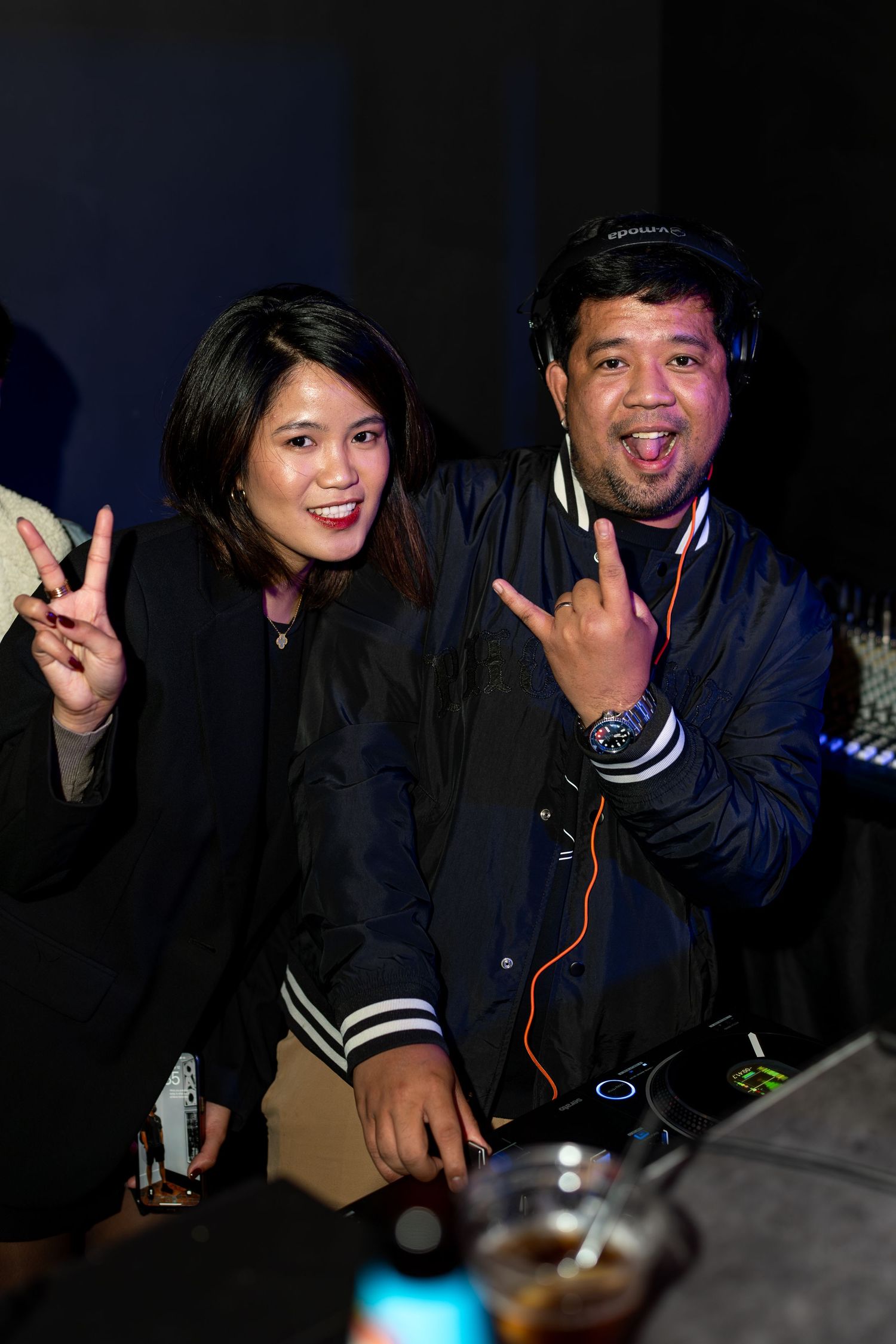 A man with DJ headphones and a woman smiling and posing together at a nightclub event.