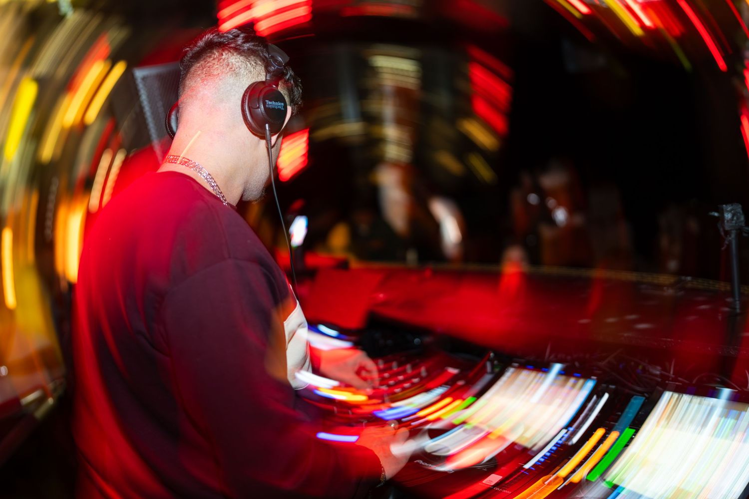 DJ wearing headphones working at turntables with colorful motion blur lights at nightclub.