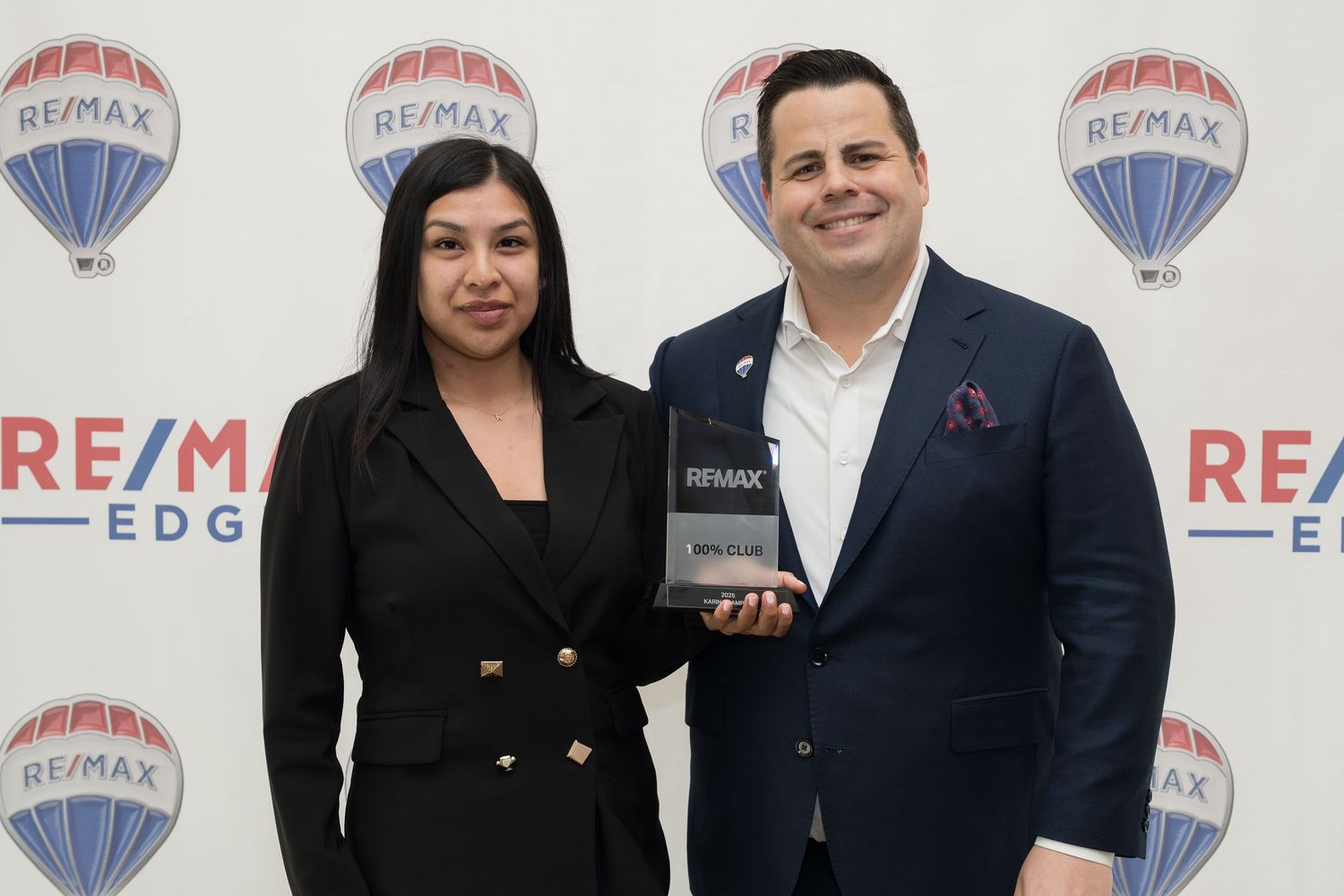 Young female RE/MAX Edge agent receives award with broker at RE/MAX event.
