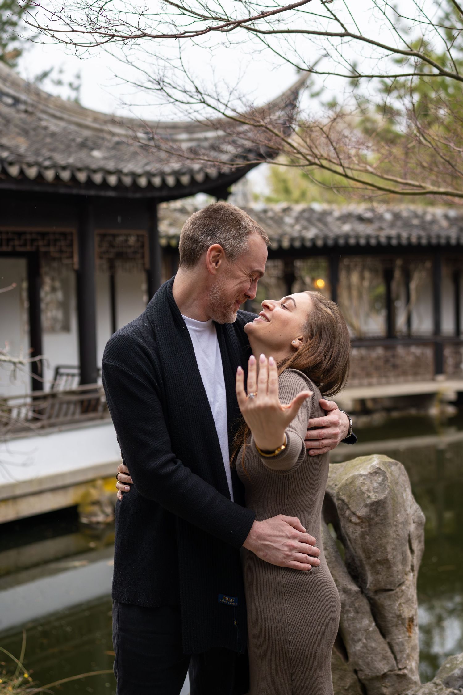Couple sharing a tender romantic moment near a pond with a traditional Chinese pagoda backdrop.
