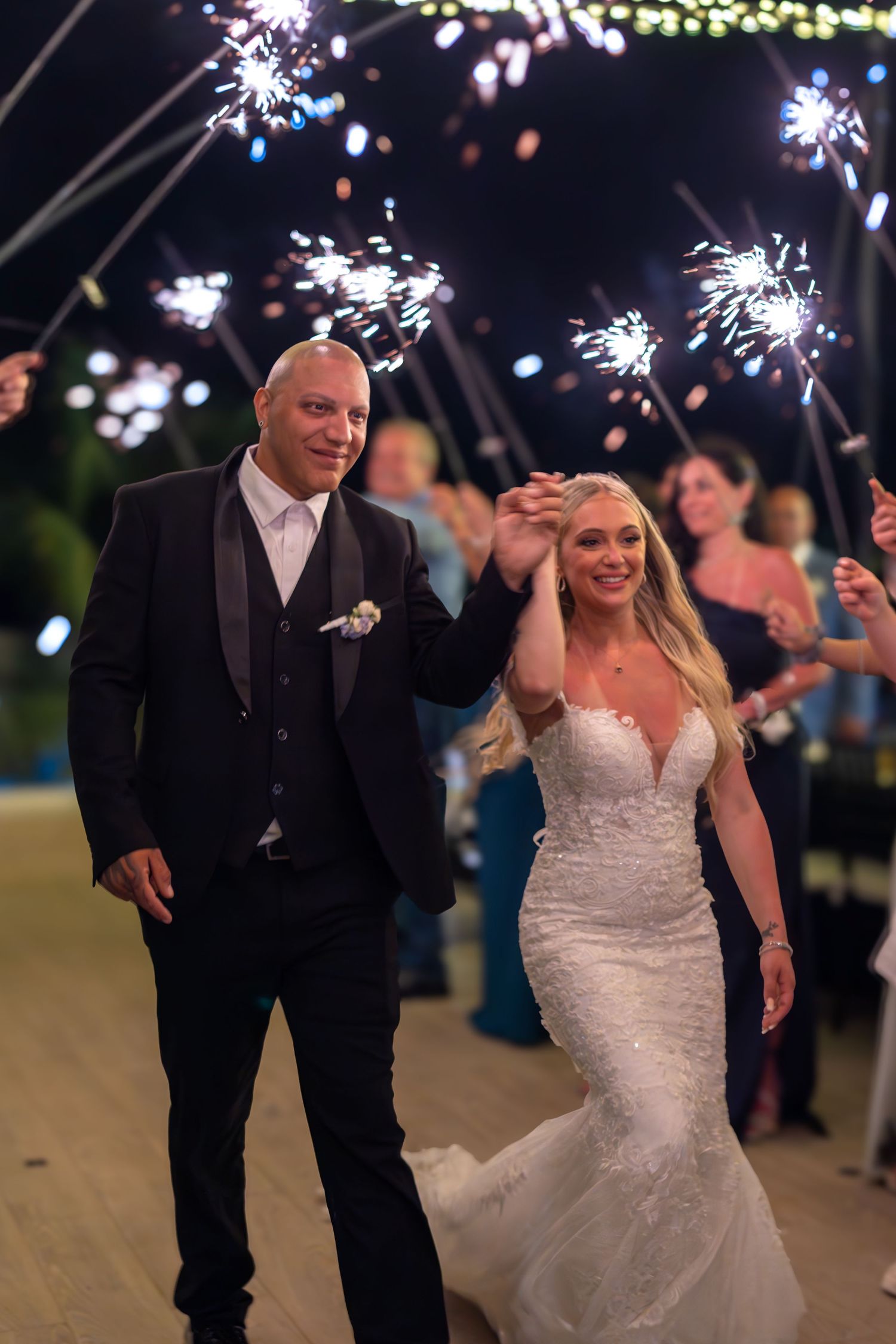 Bride and groom walk through sparkler tunnel at night during romantic outdoor wedding reception exit.