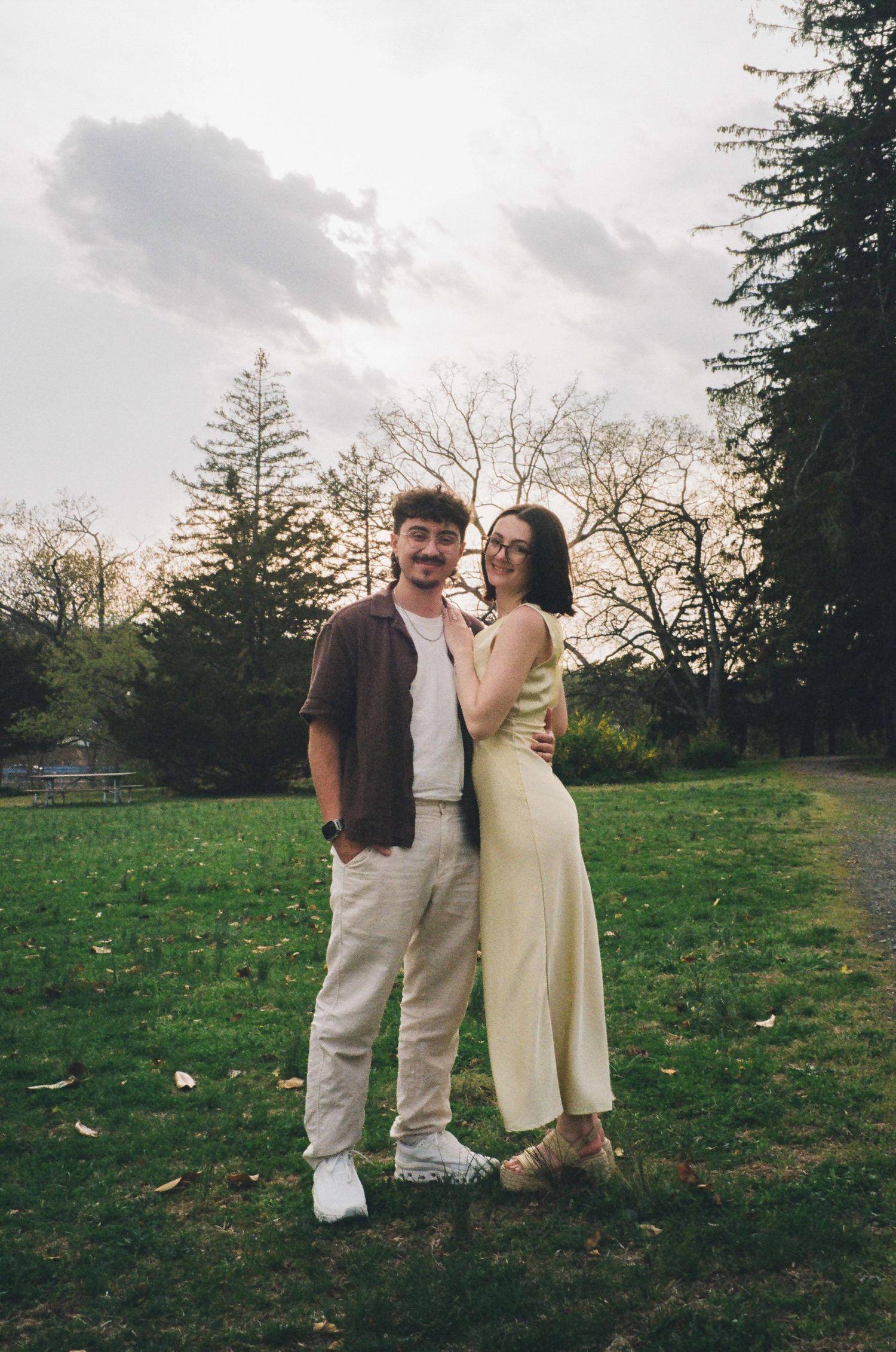 Couple embracing and smiling together on a grassy park lawn at dusk.