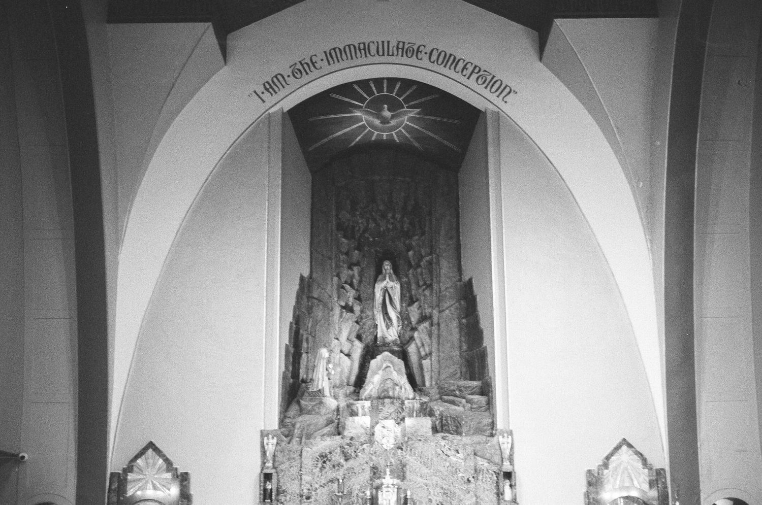 Black and white interior church photo featuring an Immaculate Conception altar with statue and arch.