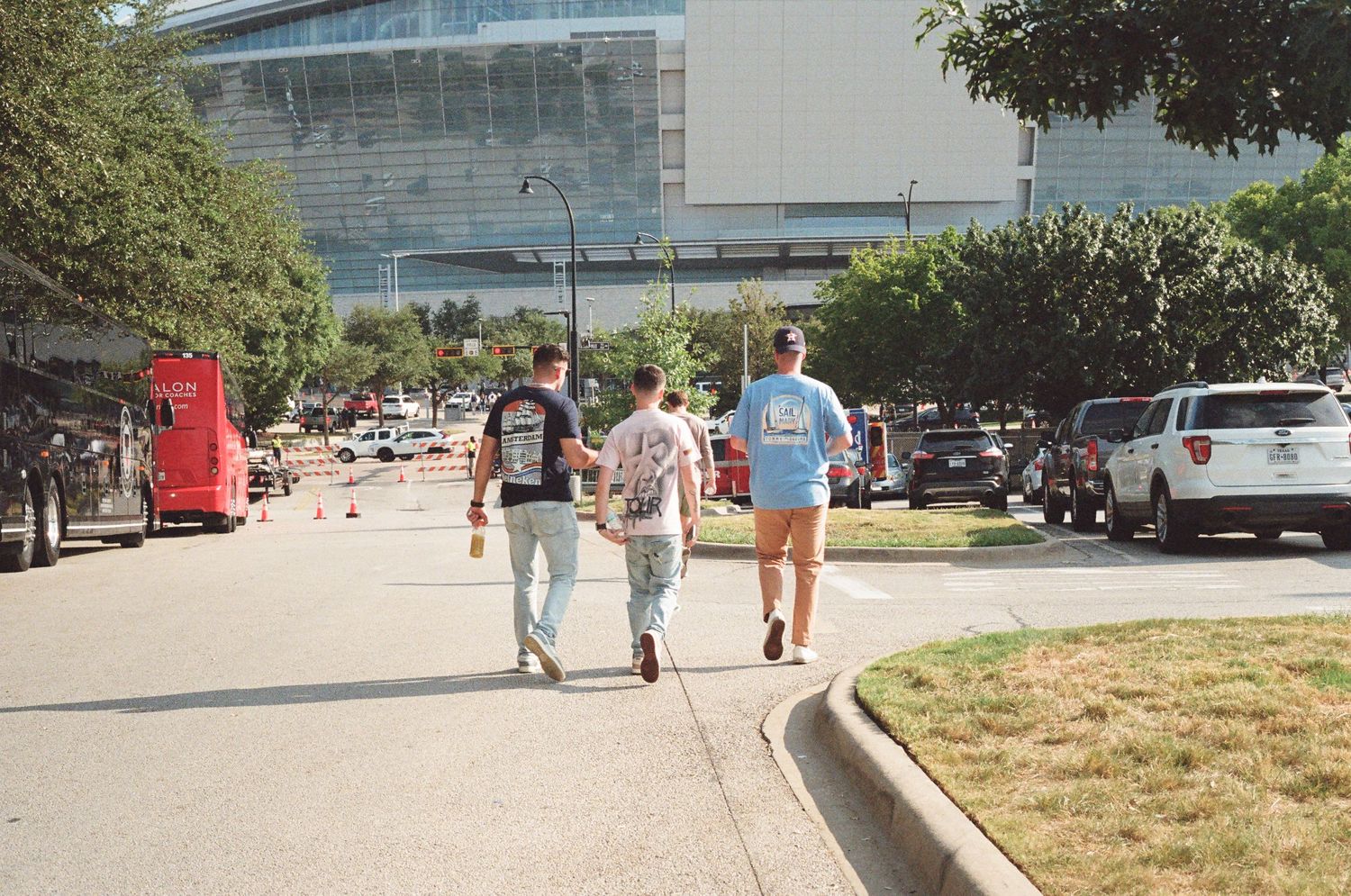 Three people walking toward AT&T Stadium on a sunny day in Arlington, Texas.