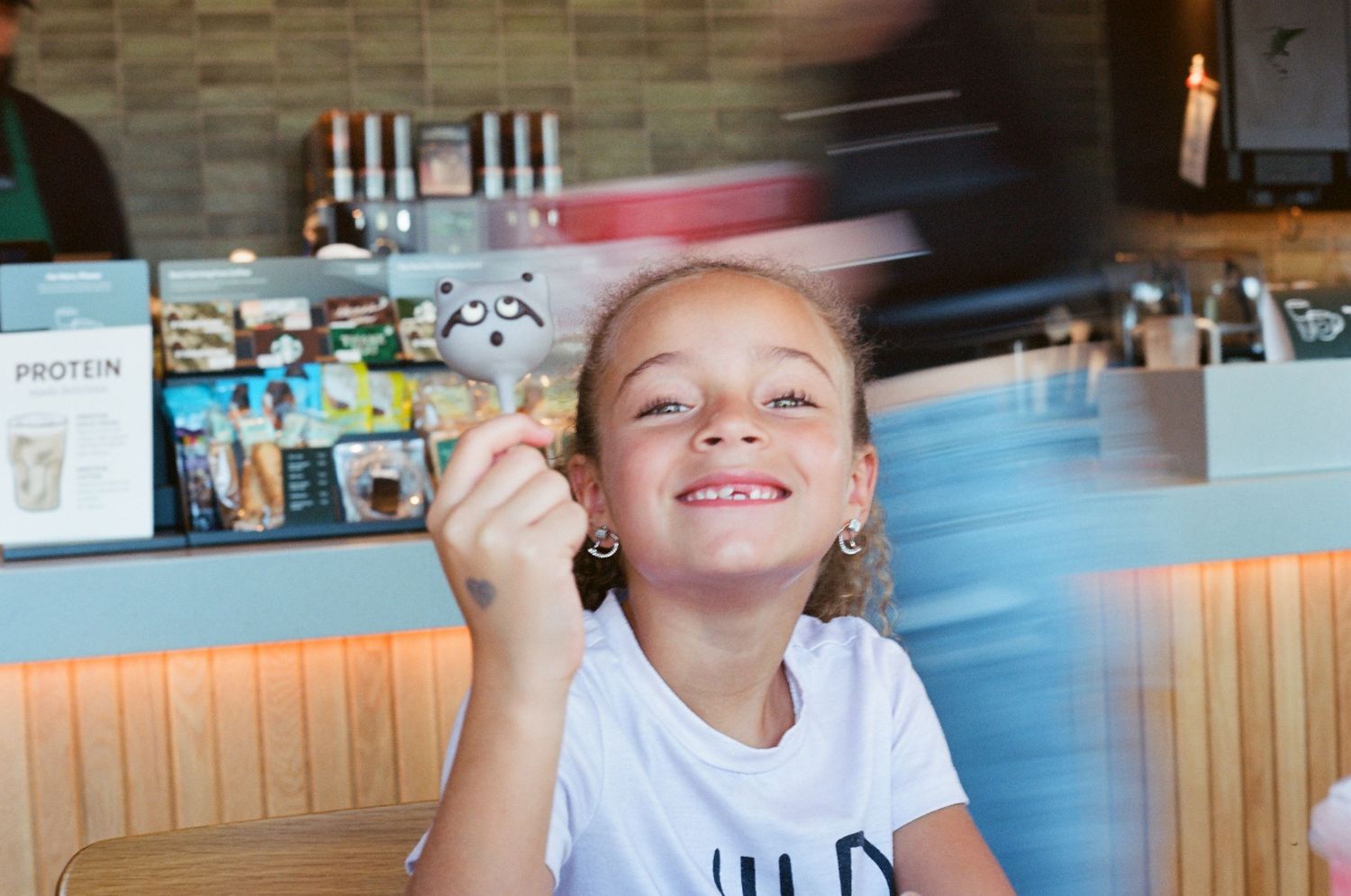 Happy young girl smiling and holding a treat inside a bright modern cafe restaurant.