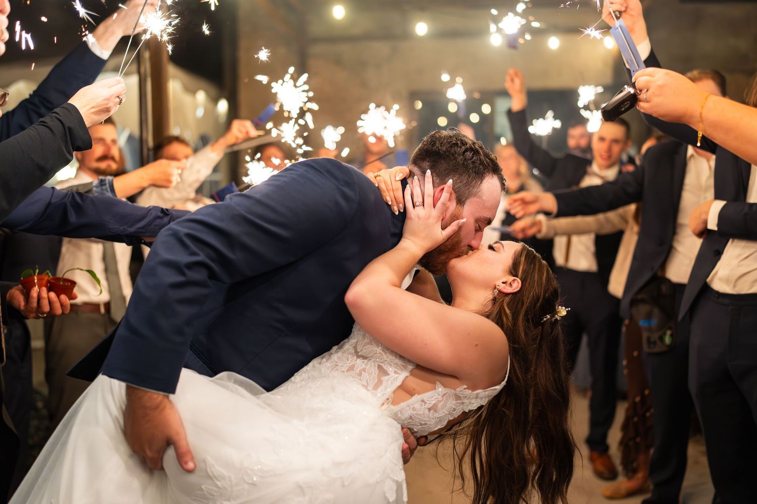 Newlyweds share a dramatic dip kiss during sparkler send-off at their wedding celebration.