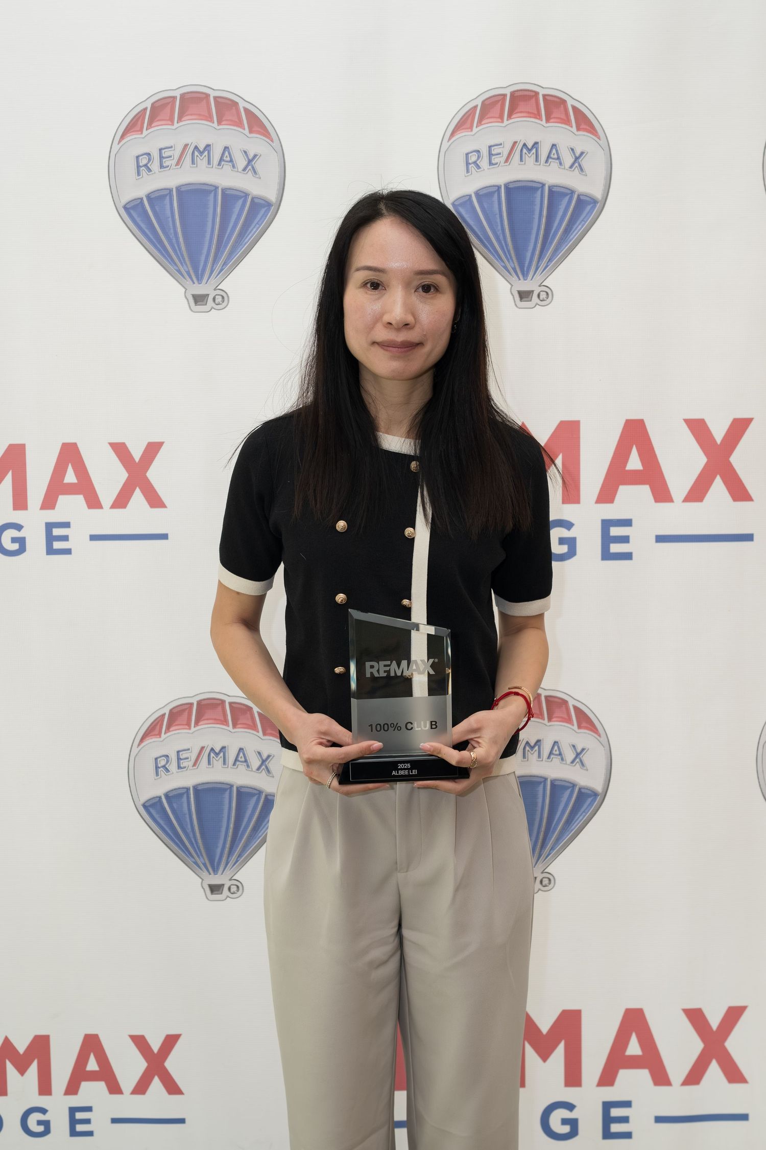 RE/MAX Edge female agent holds RE/MAX achievement trophy at awards ceremony.